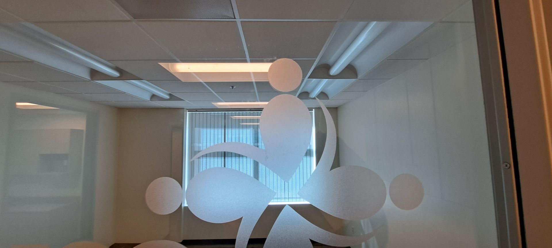 Office hallway with frosted glass door featuring white circular decals and a window in the background