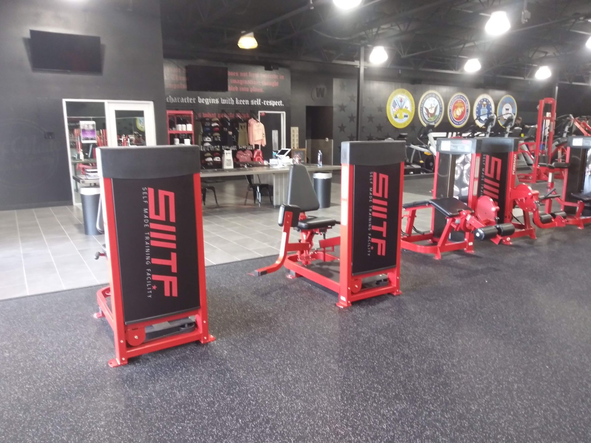 Red and black gym with strength machines and rubber flooring in a spacious workout area.