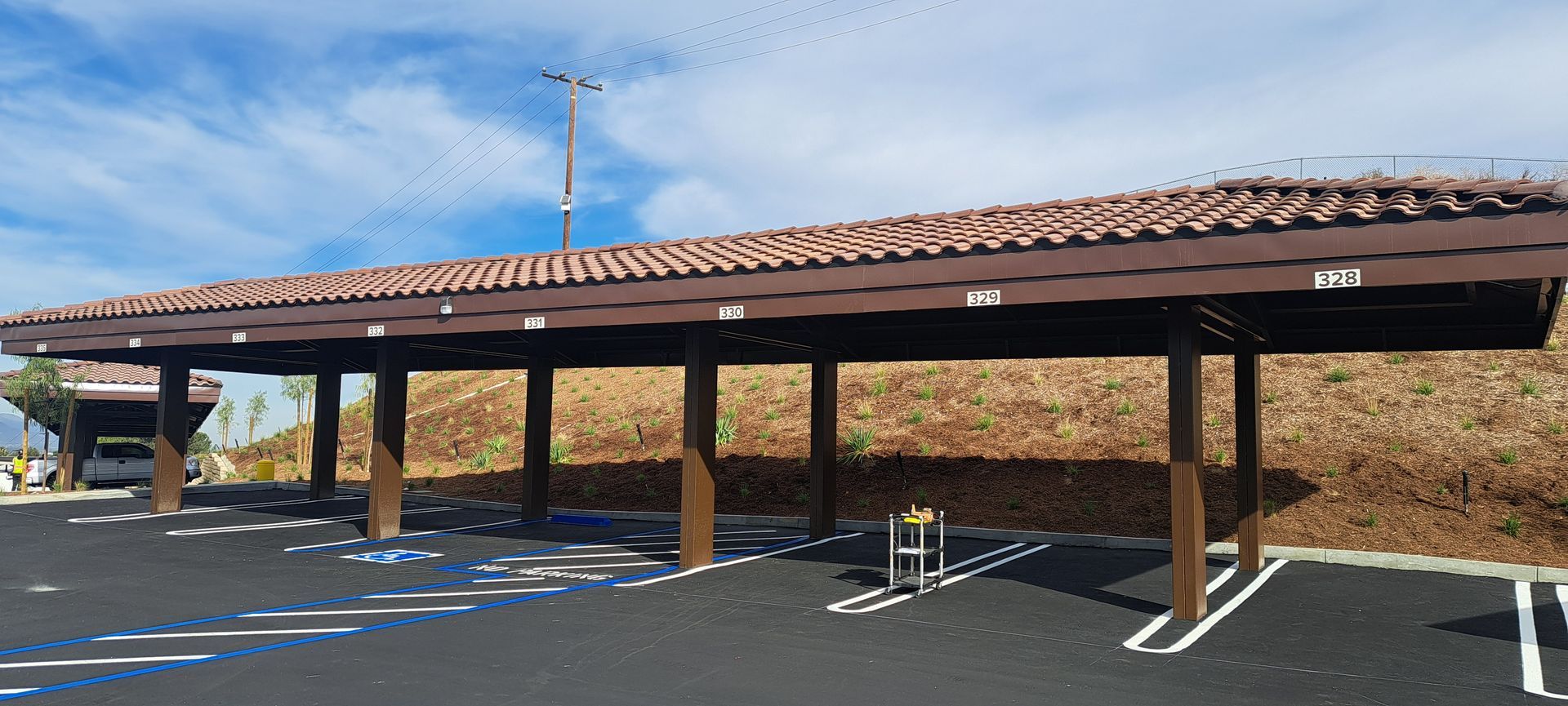 Covered parking area with terracotta roof and solar panels in a mostly empty lot