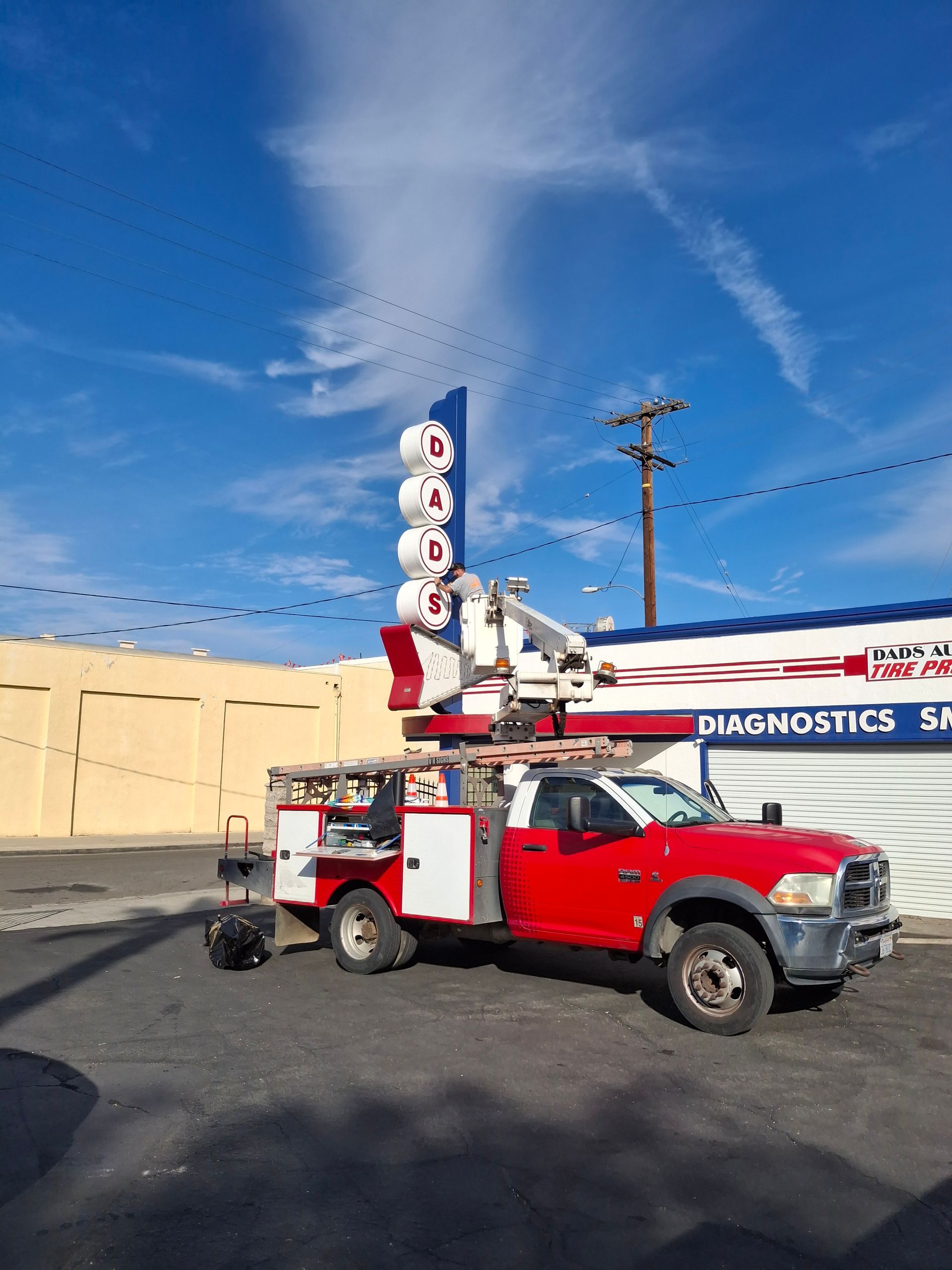 Red utility truck with tall diagnostic sign parked outside a building under a blue sky