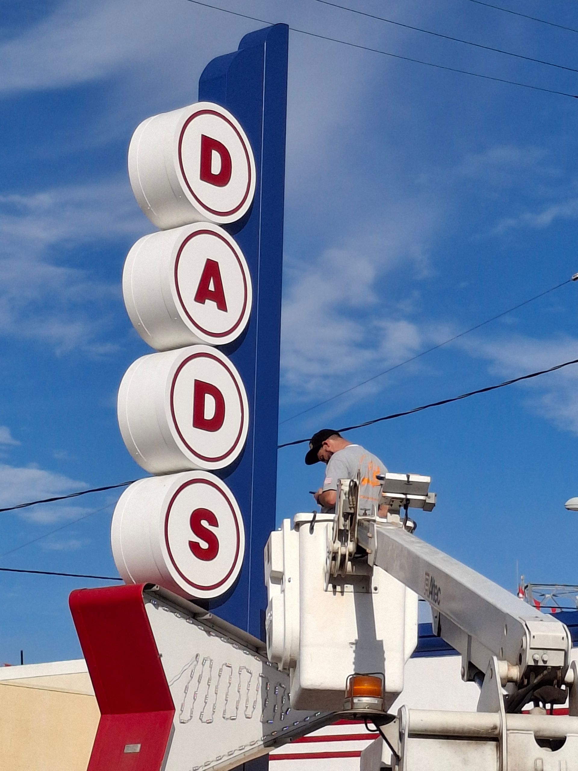 Vintage DADS sign against blue sky, with a worker on a lift near the top.
