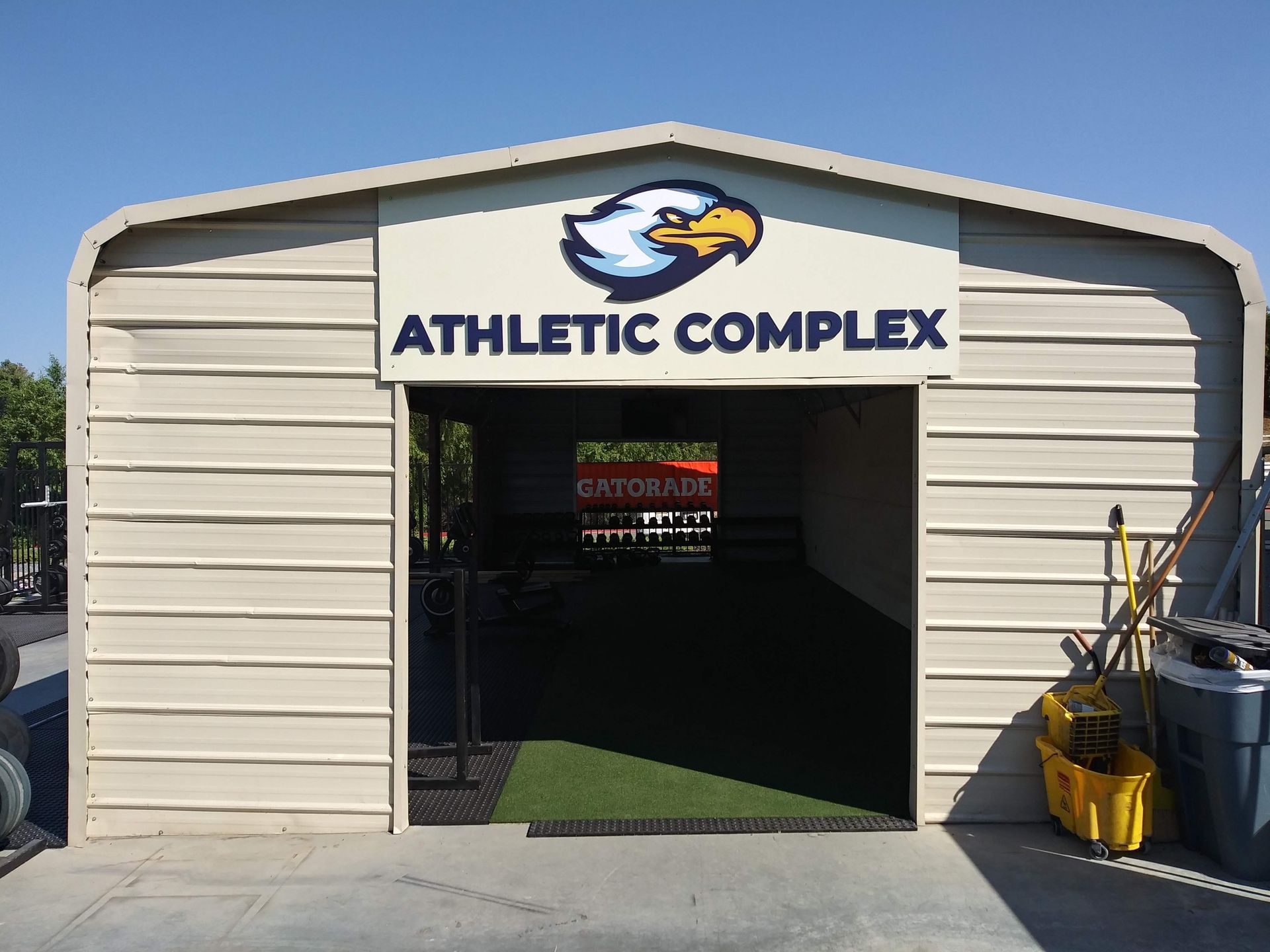 Small beige athletic complex building with open entrance and eagle logo above the door