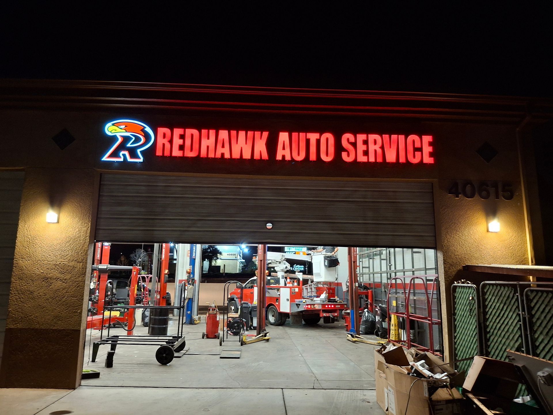 Auto service garage entrance at night, with red “REDHAWK AUTO SERVICE” sign and cars inside.