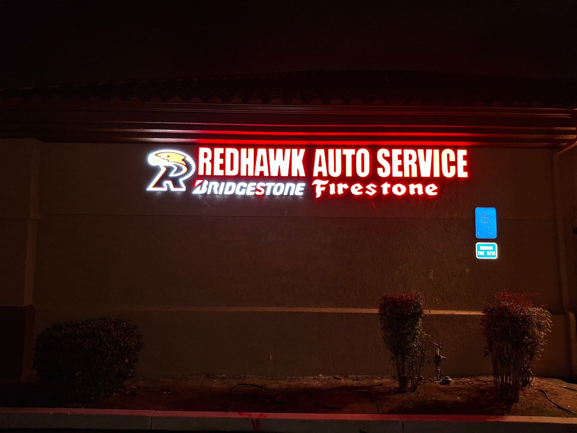Redhawk Auto Service and Firestone illuminated sign at night on a building exterior