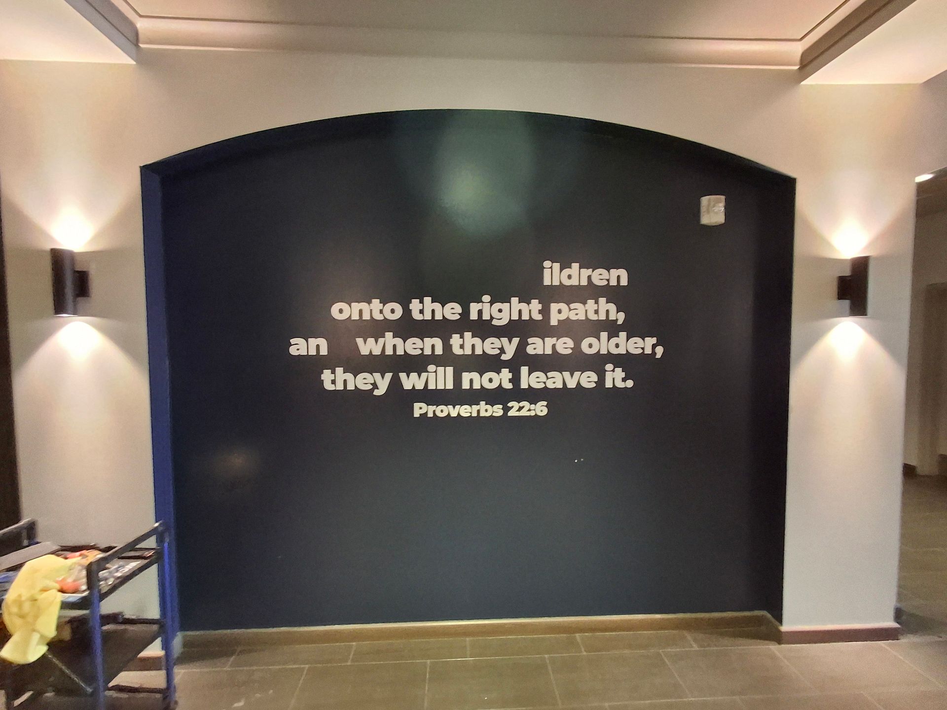 Dark wall with Bible verse text in a softly lit hallway or lobby.