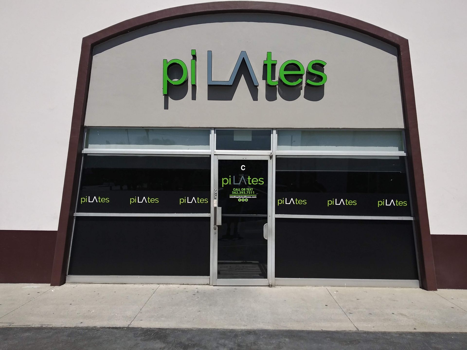 Storefront with a green-and-black sign, large windows, and a centered glass entrance under an arched facade