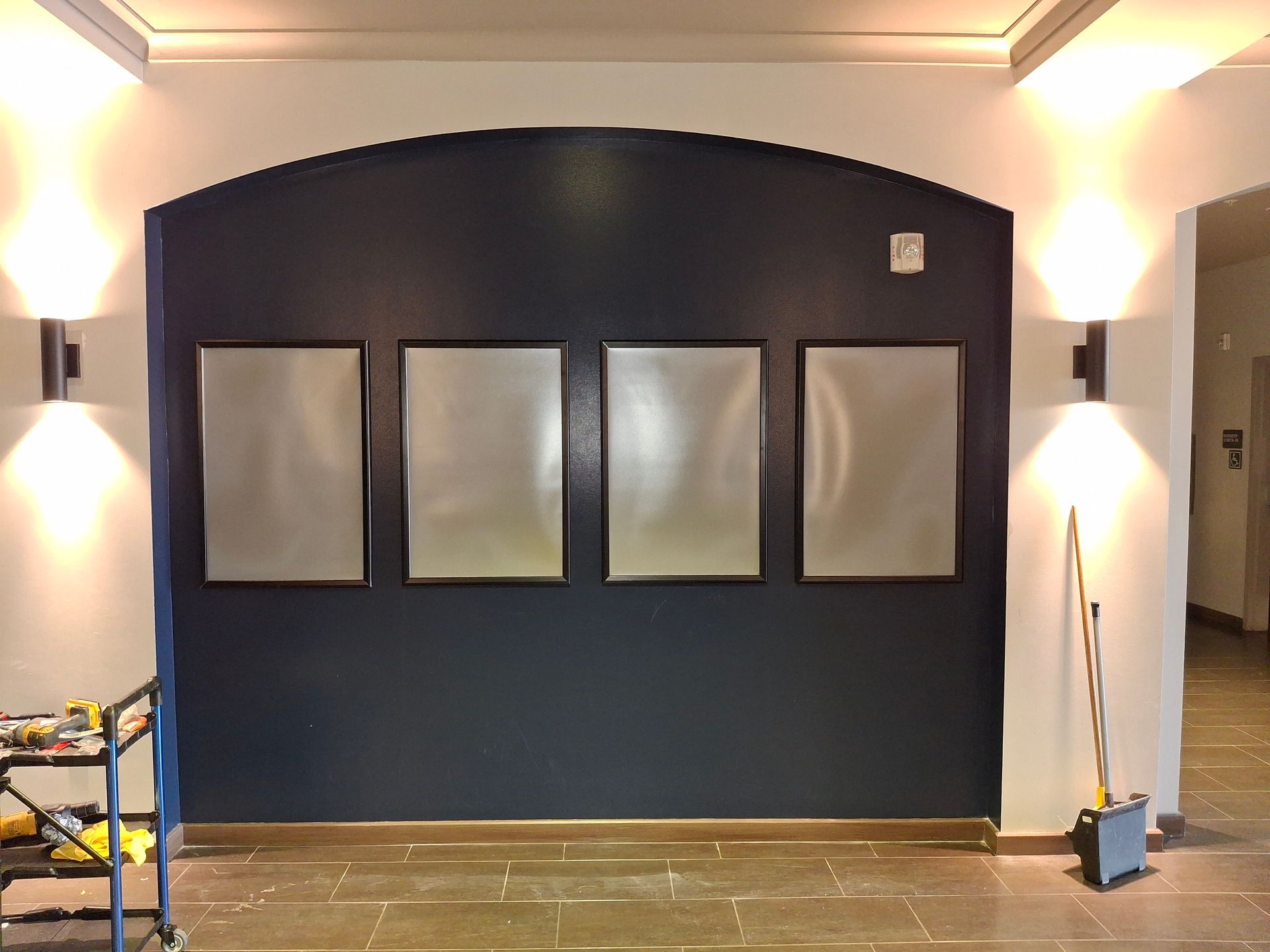 Empty room with dark accent wall, four windows, and wall sconces on both sides.