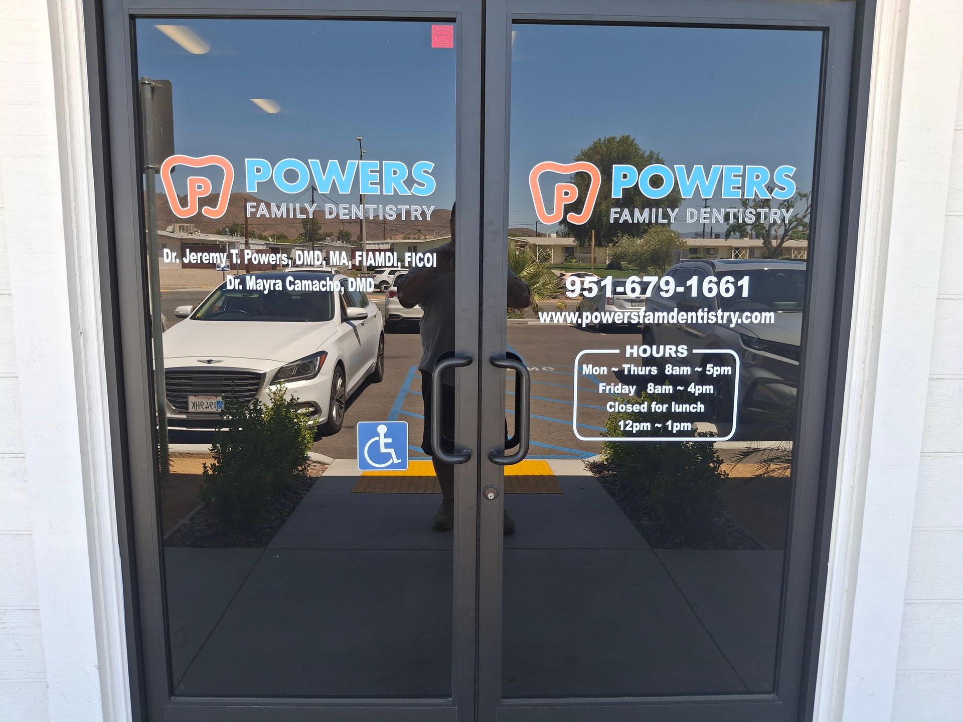 Glass storefront doors for Powers Family Dentistry with logo, phone number, and accessibility sign