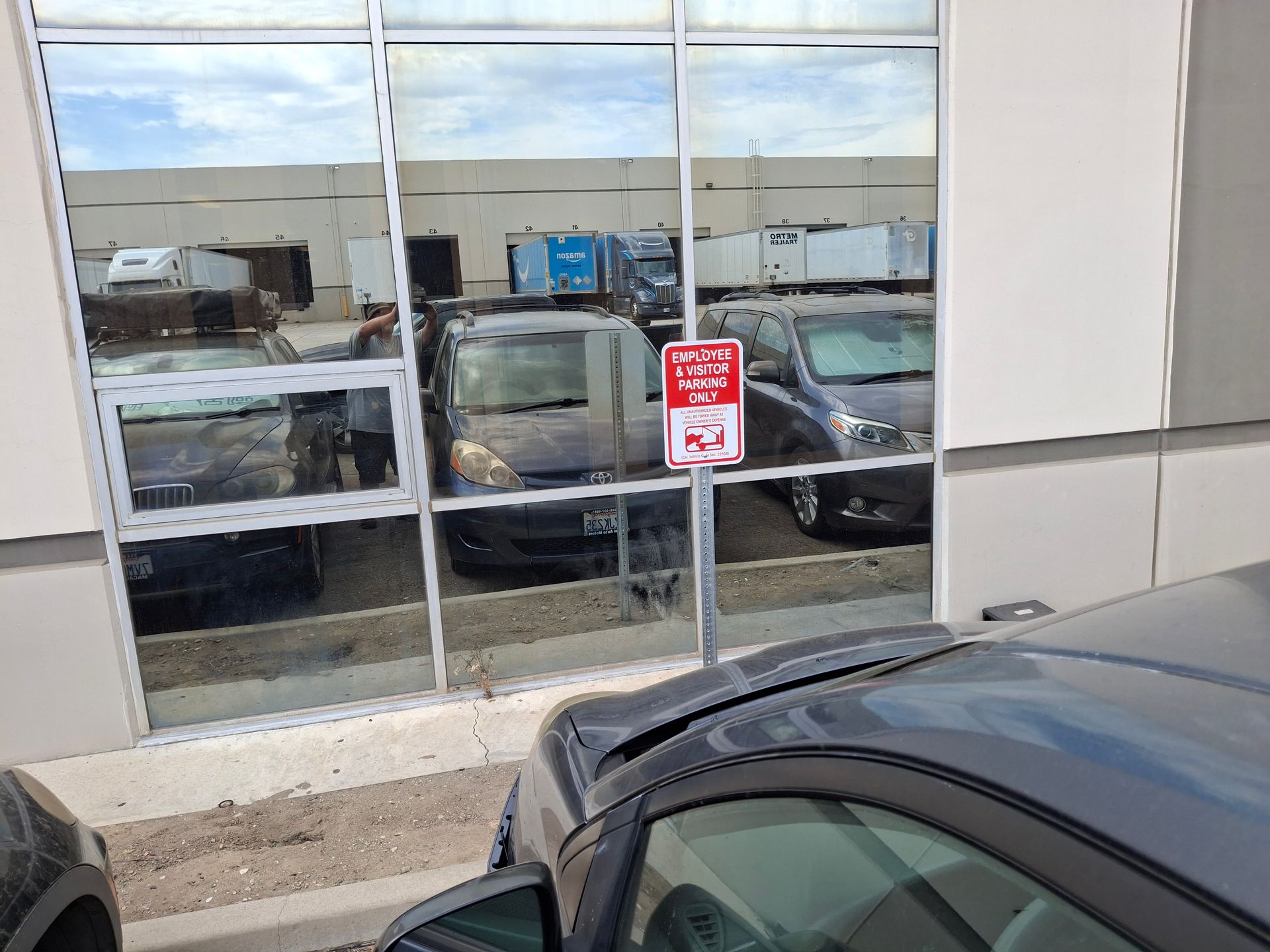 Car dealership windows reflecting parked cars, with a red warning sign on the glass.