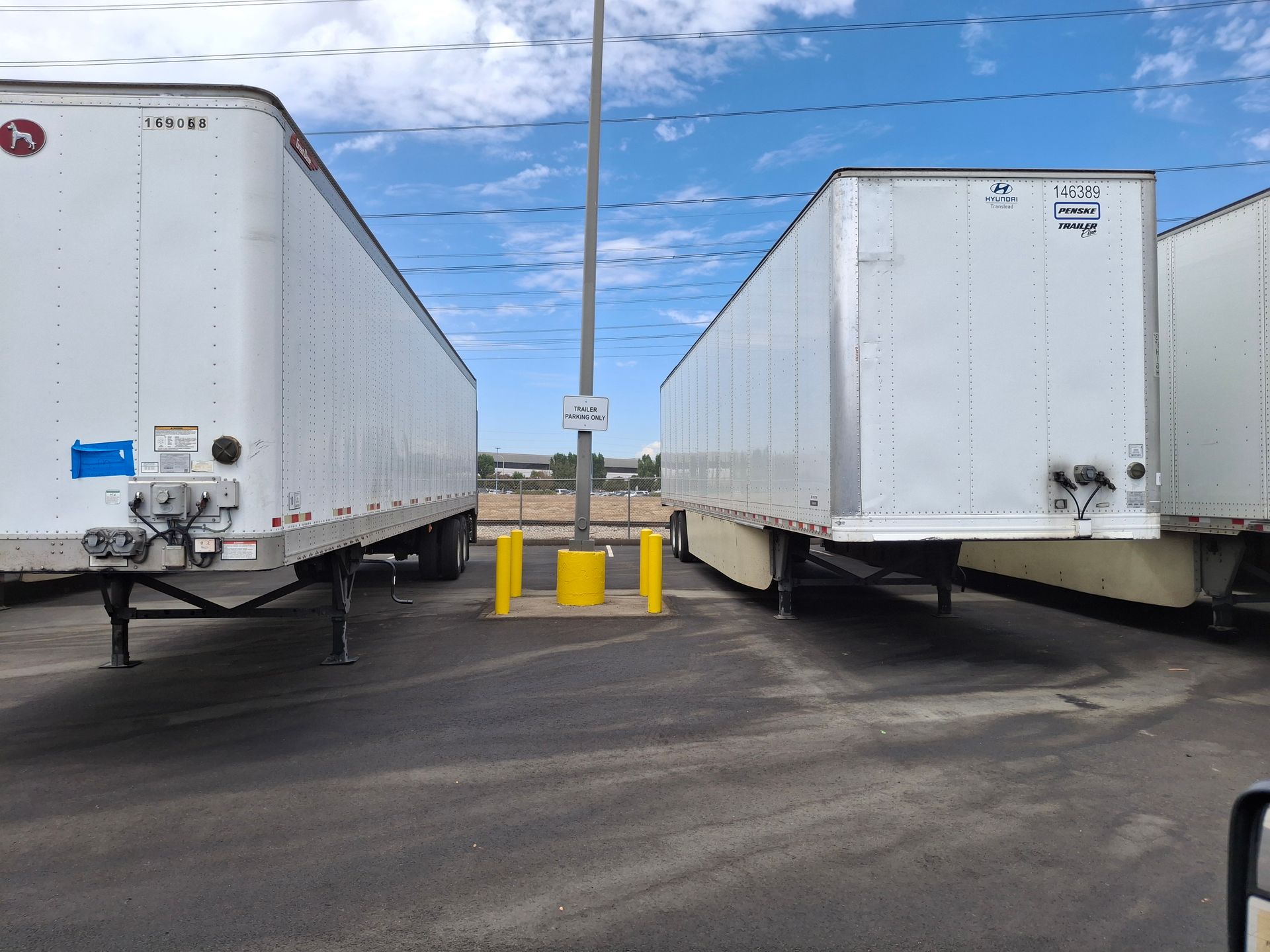 Two white semi-trailers parked on either side of a narrow asphalt lane under a blue sky.