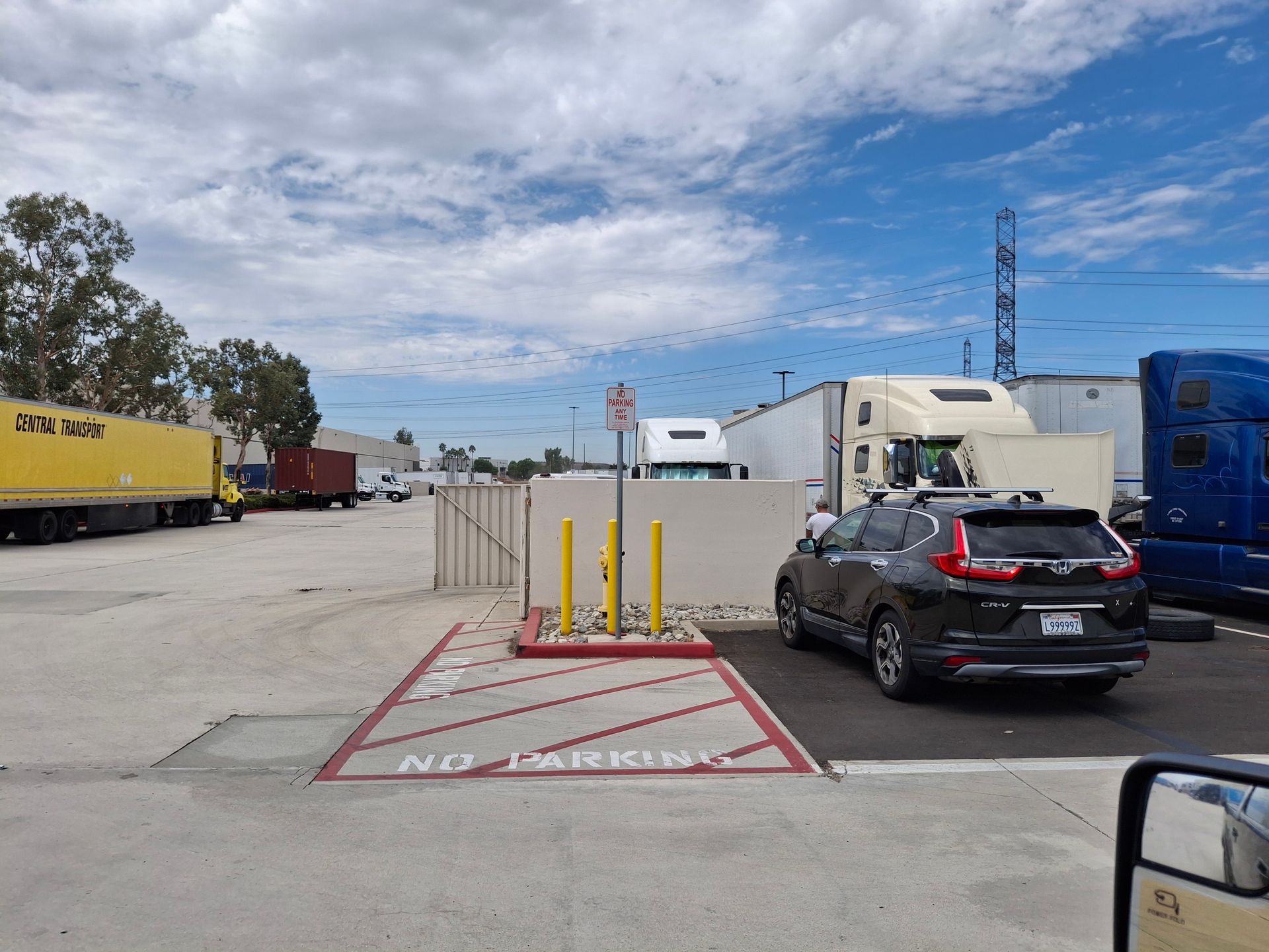 Truck yard with parked semi-trailers, a black SUV, and a fenced no-parking zone under a cloudy sky