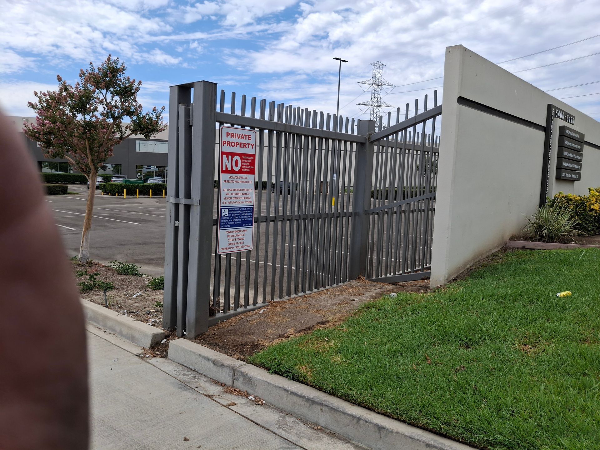 Metal security gate with warning signs beside a sidewalk and grassy area