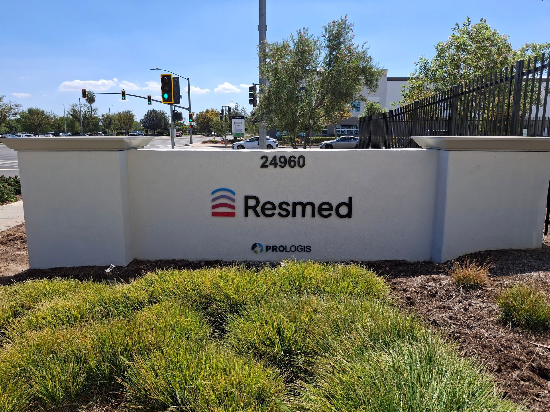 Resmed office sign on a white stone wall with landscaping and a street intersection in the background