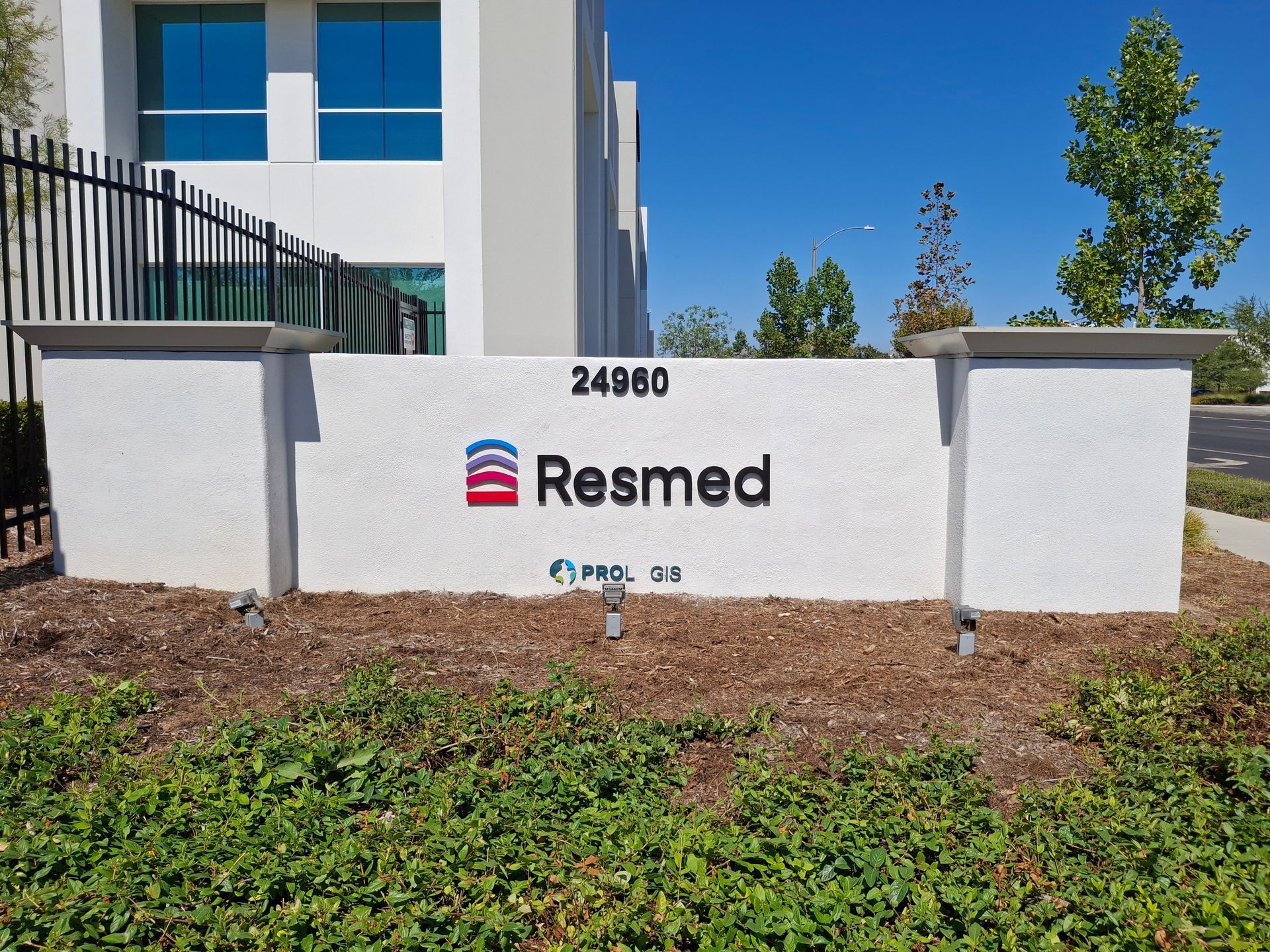 Resmed office sign on a white wall outside a modern building, with trees and landscaping