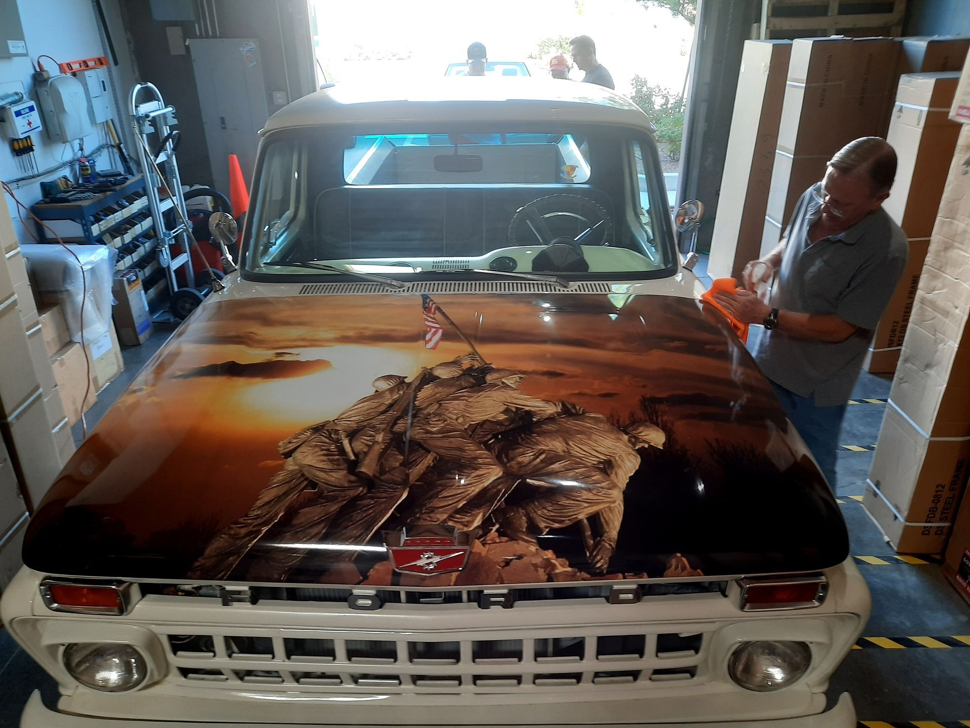 Vintage pickup truck in a garage, with a large rusted hood and a man standing beside it.