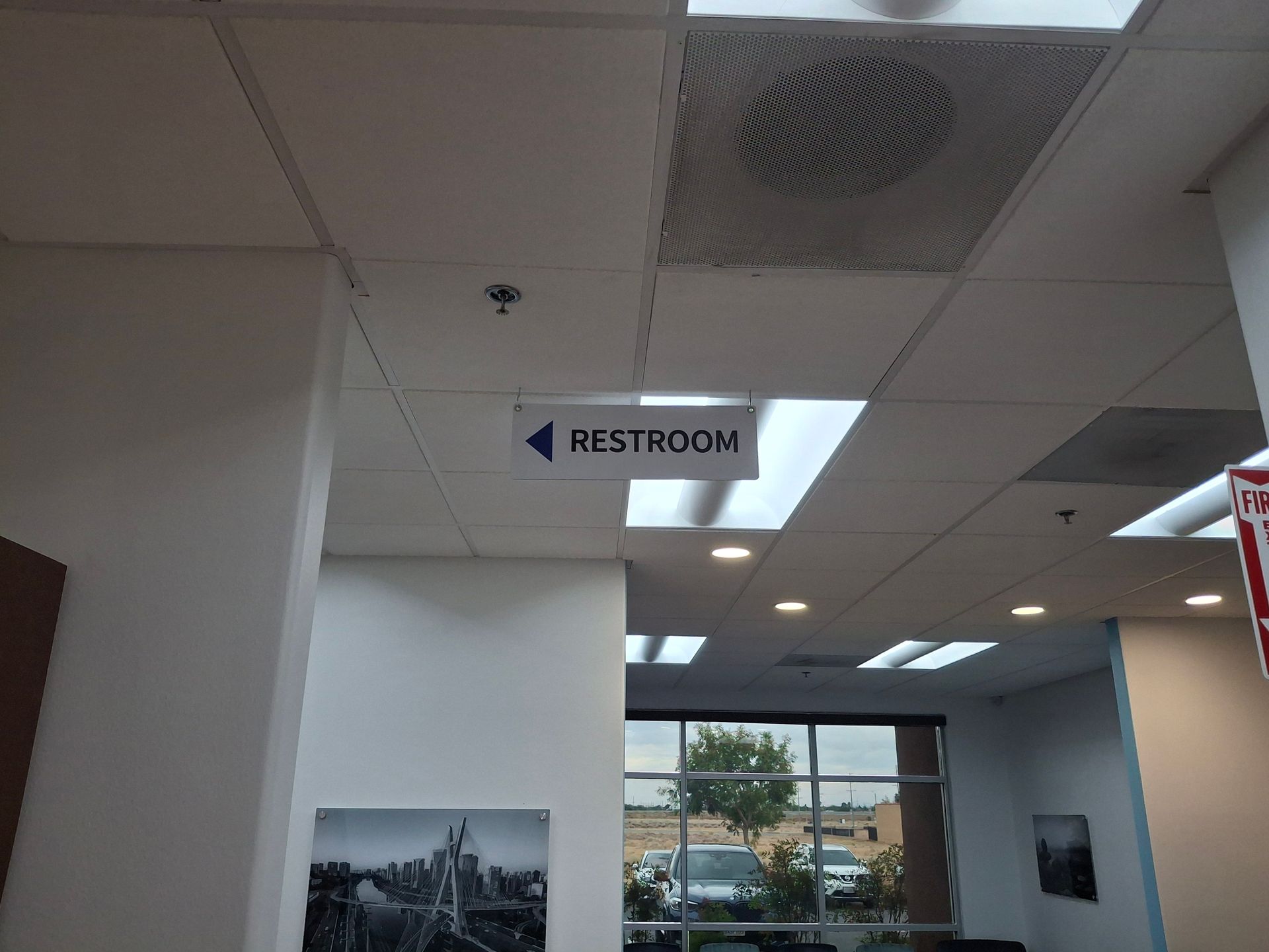Office hallway sign pointing to restroom under ceiling lights