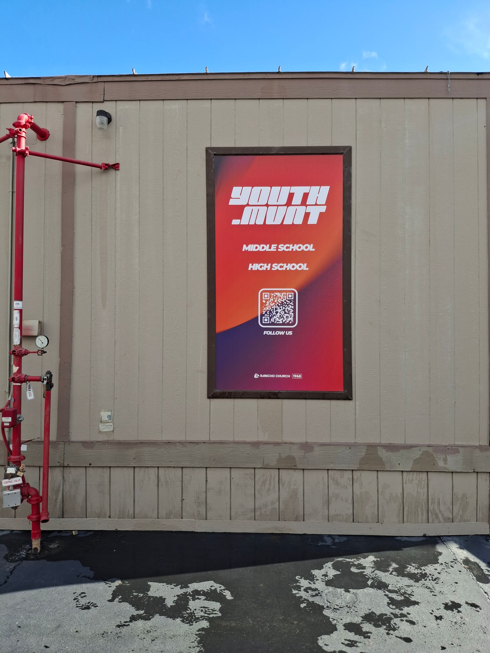 Red wall poster on a beige building exterior with a QR code and white text.
