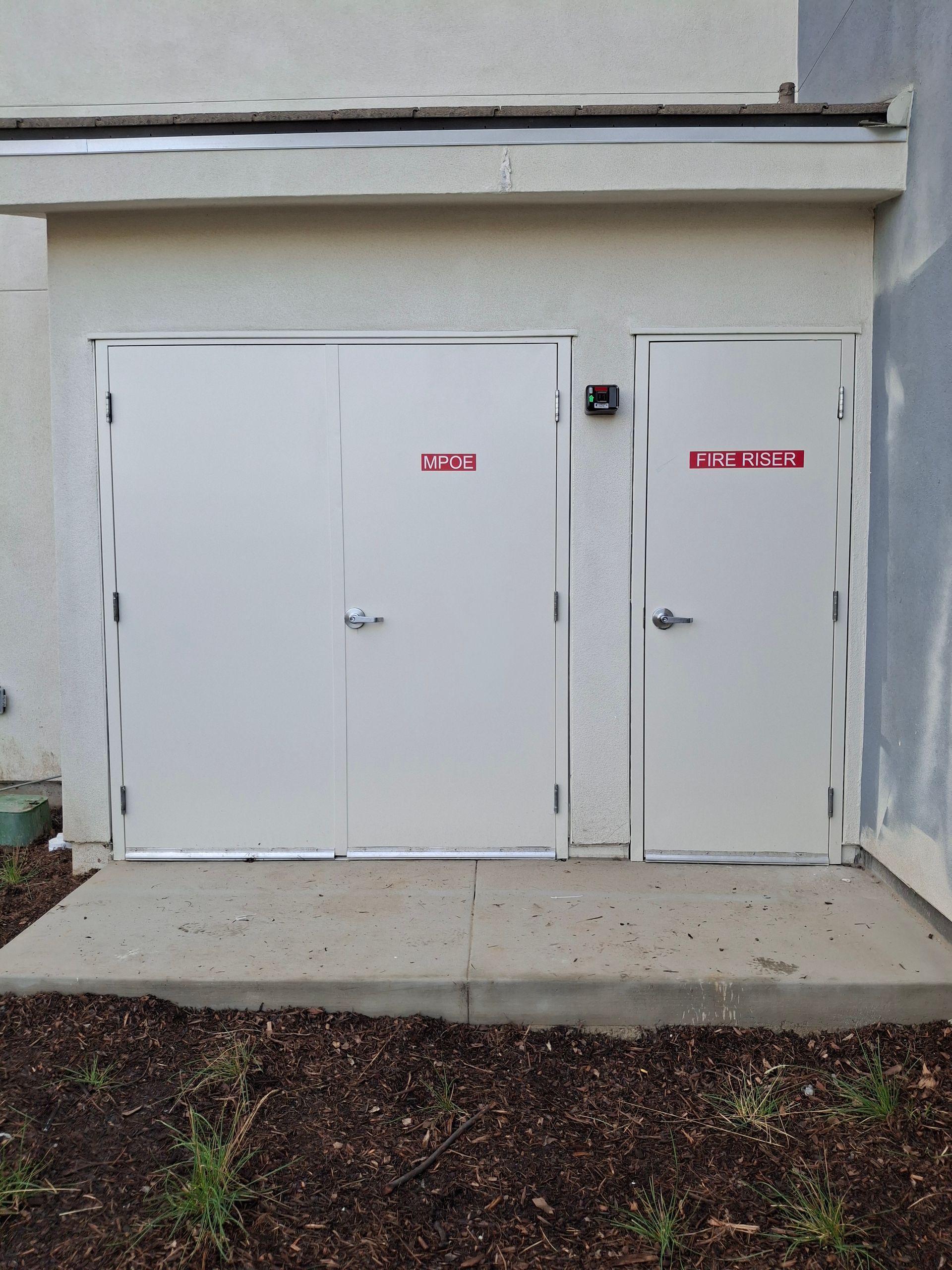 White utility double doors and a smaller side door on a plain building exterior.