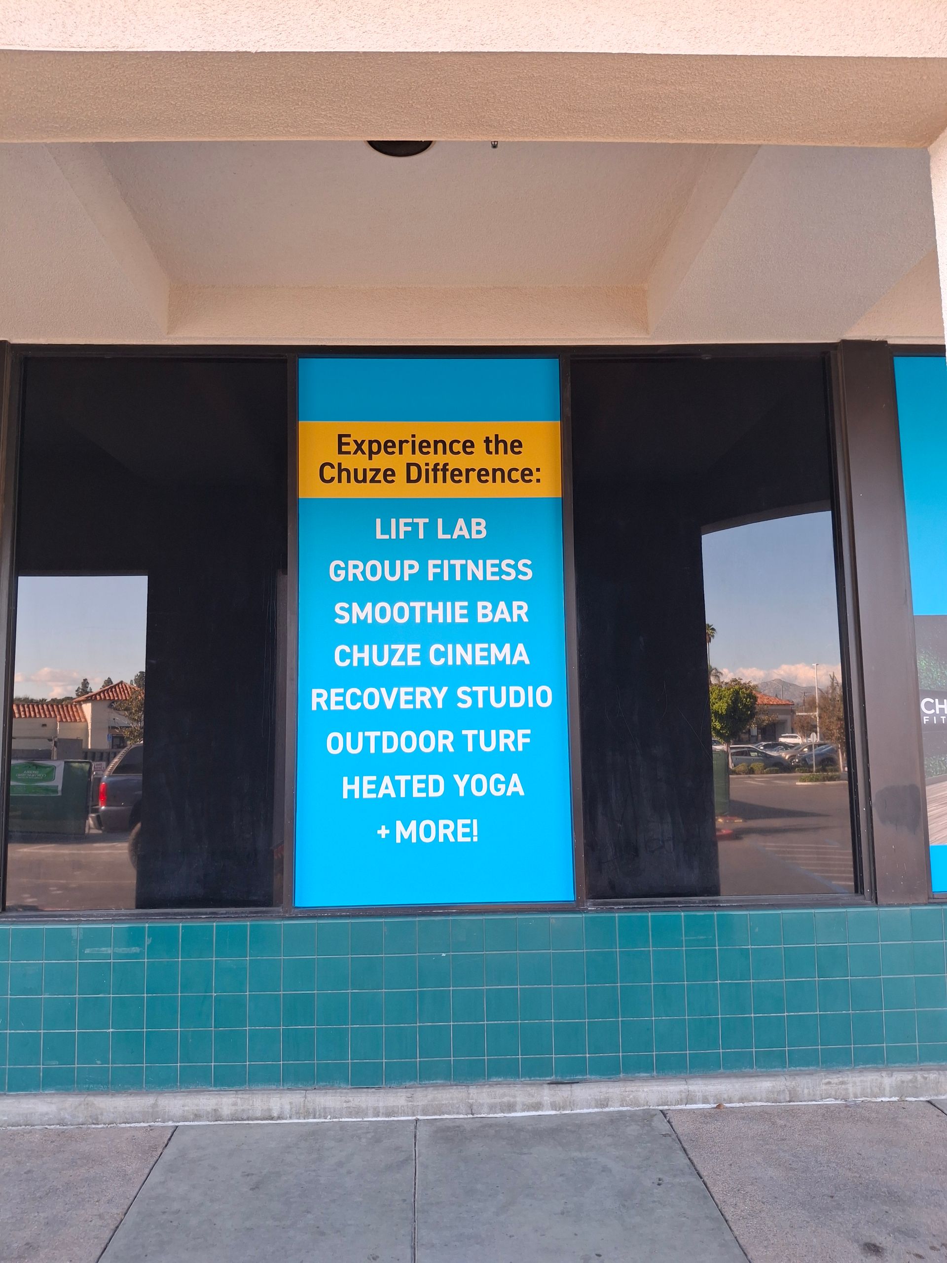 Storefront window sign listing classes: lift lane, group fitness, smoothie bar, cycle class, recovery studio, outdoor turf, history tour.