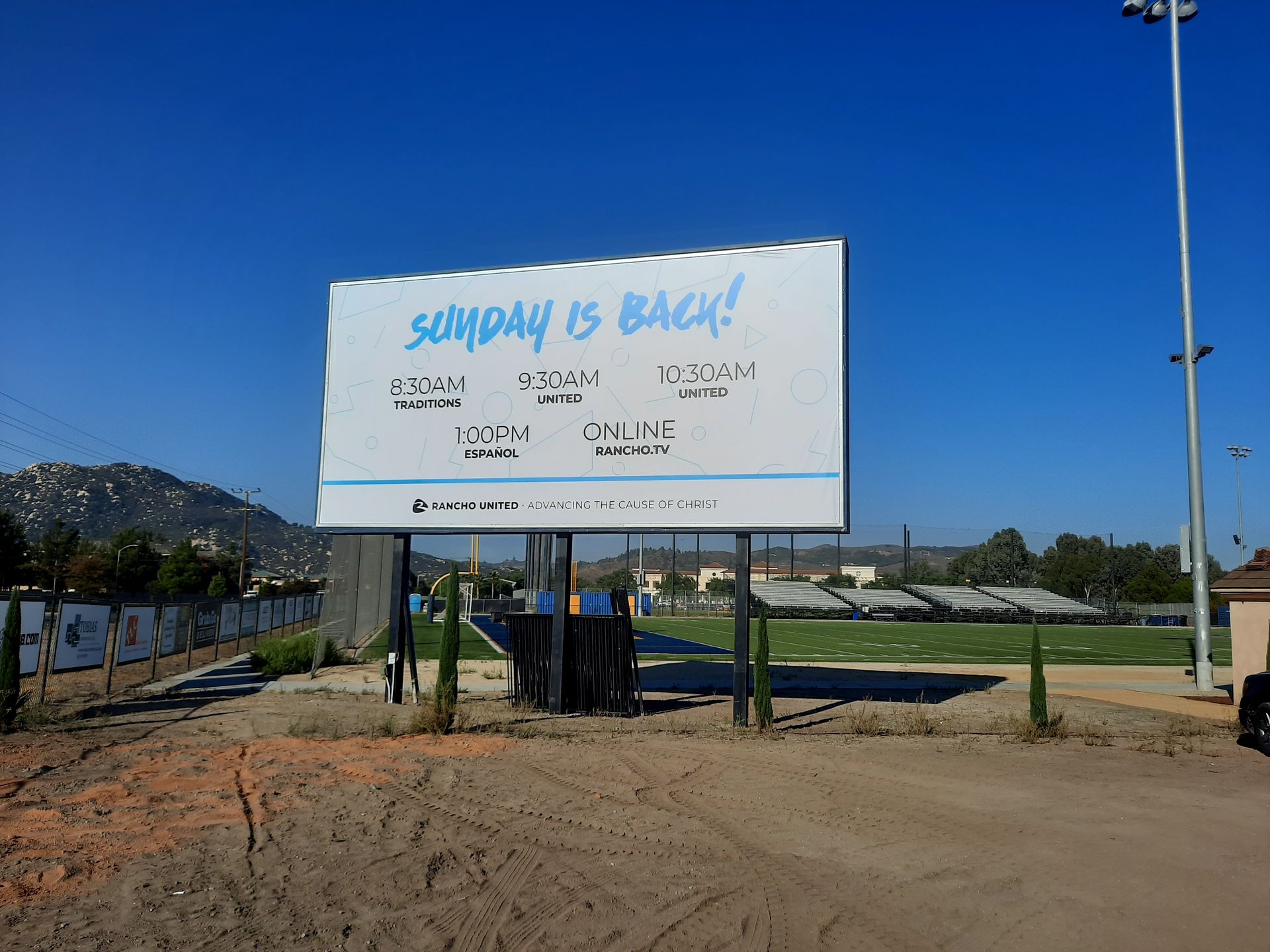 Billboard sign in a dusty lot under a clear blue sky, with mountains in the background.