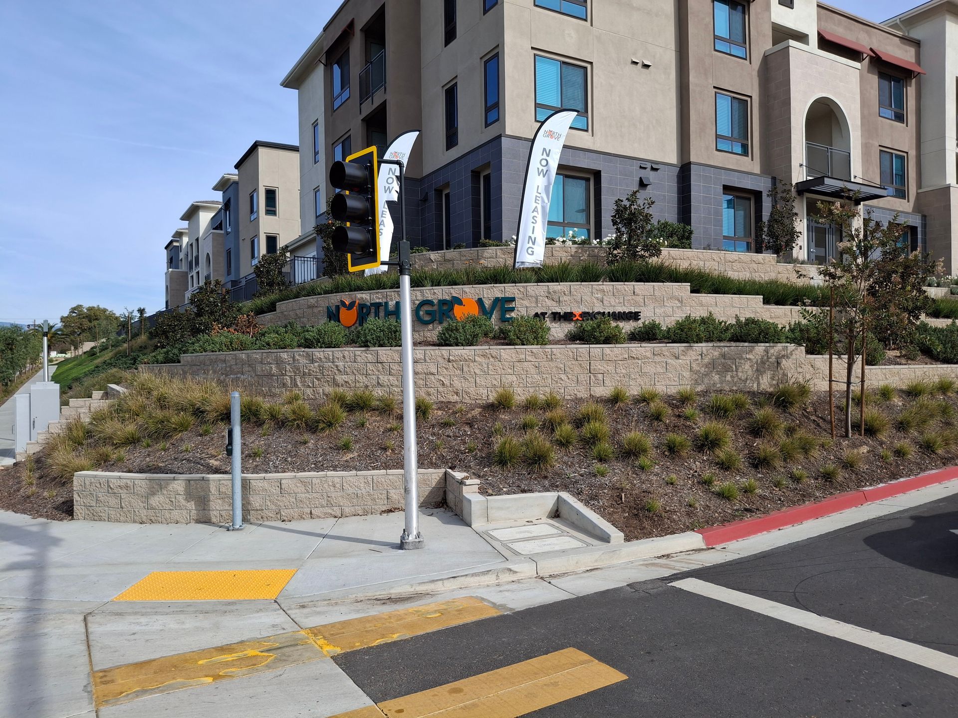 Modern apartment building with landscaped hillside, flags, and a sidewalk corner with curb ramps