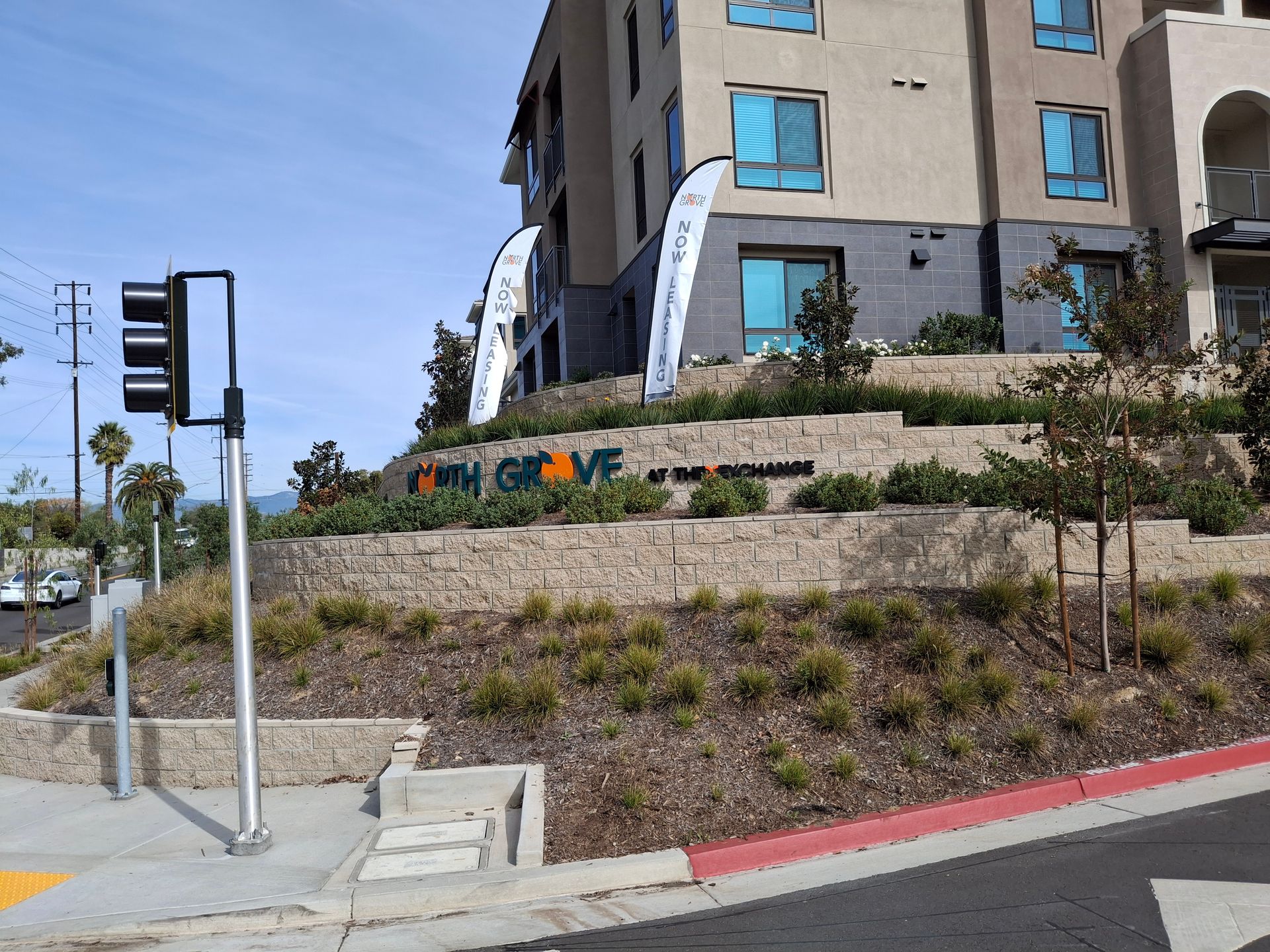 Modern apartment building on a landscaped hillside beside a street corner and traffic light.