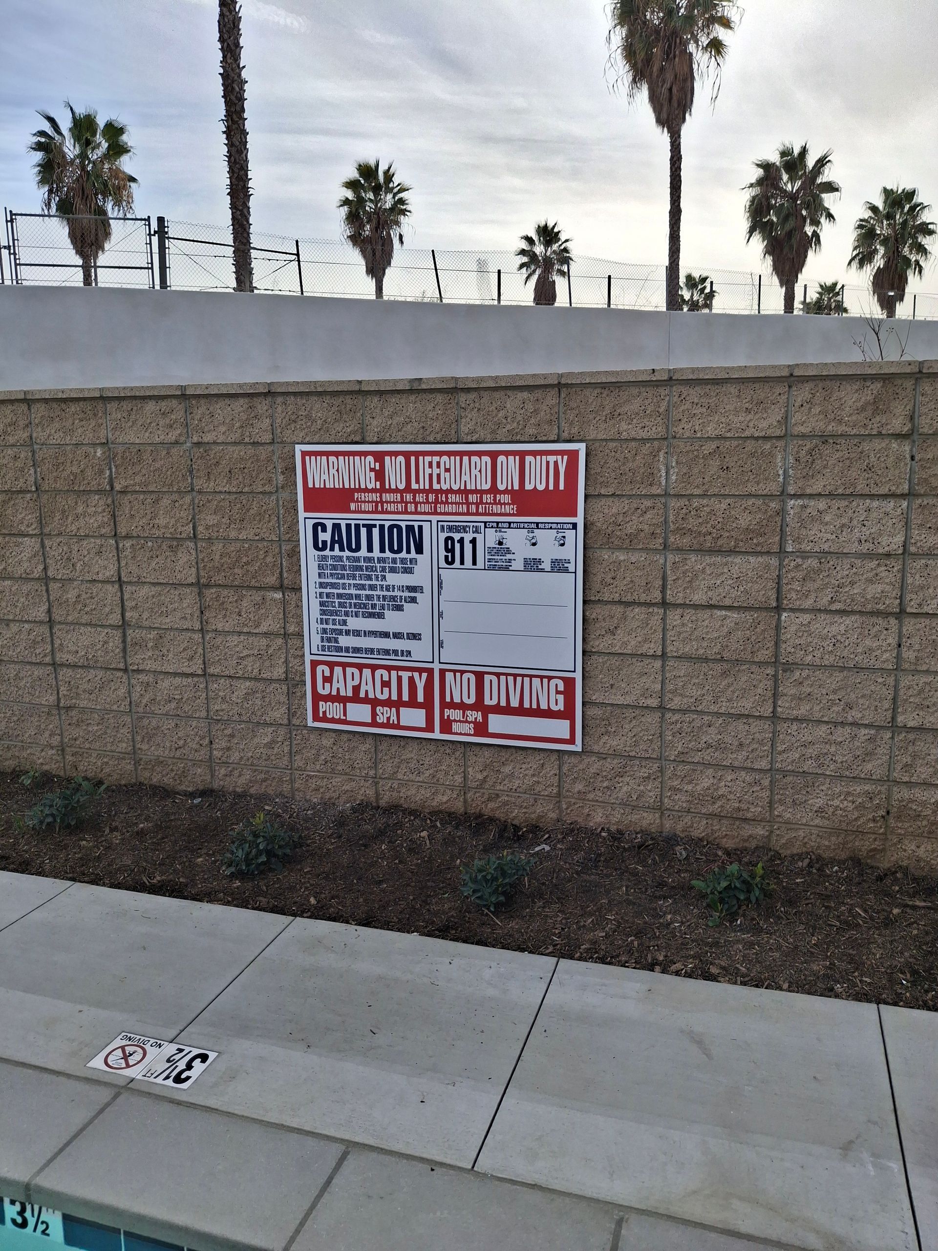 Closed sign on a tan block wall beside a sidewalk, with palm trees in the background.