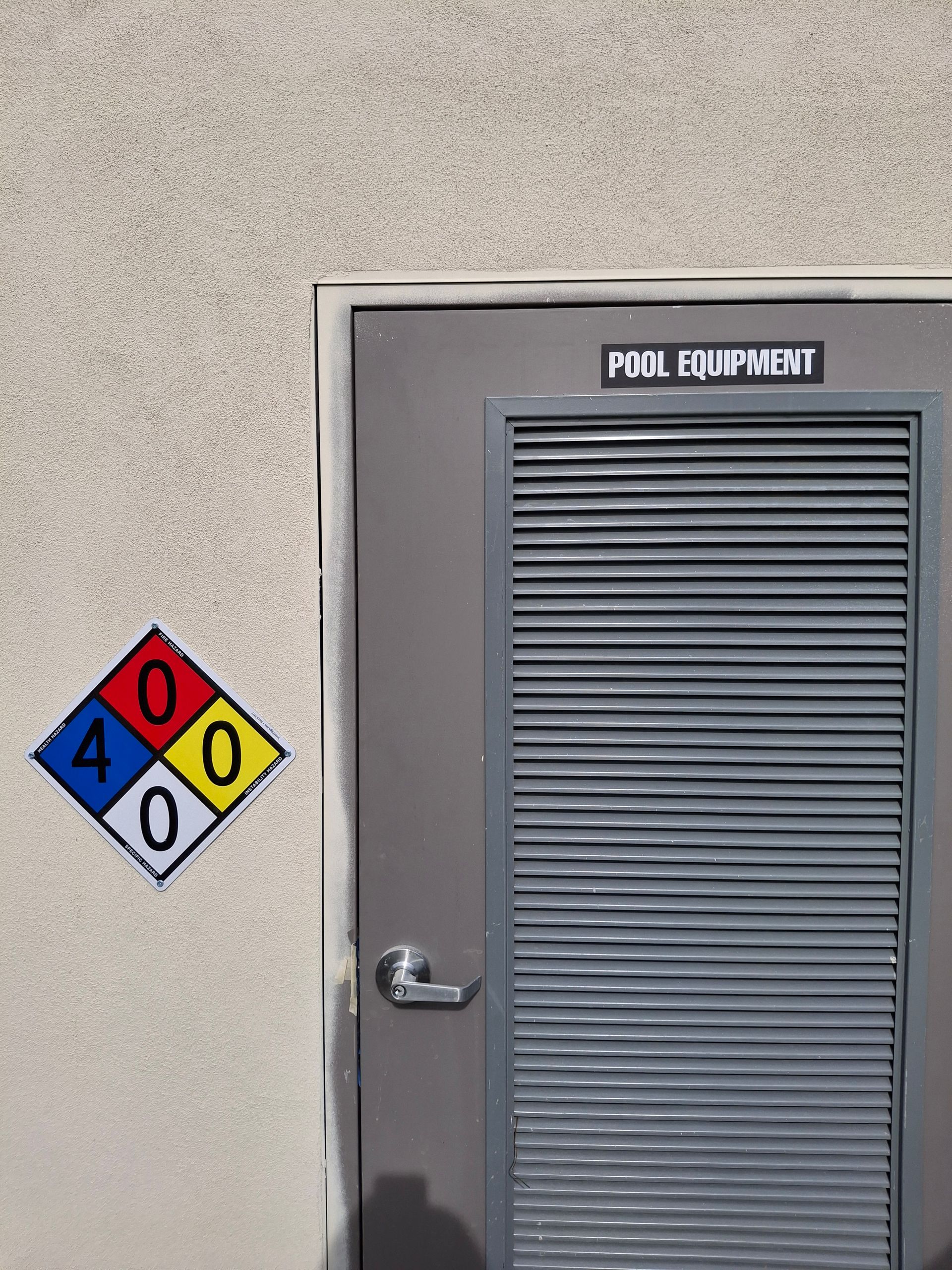 Pool equipment room door with hazardous materials placard on a beige wall.