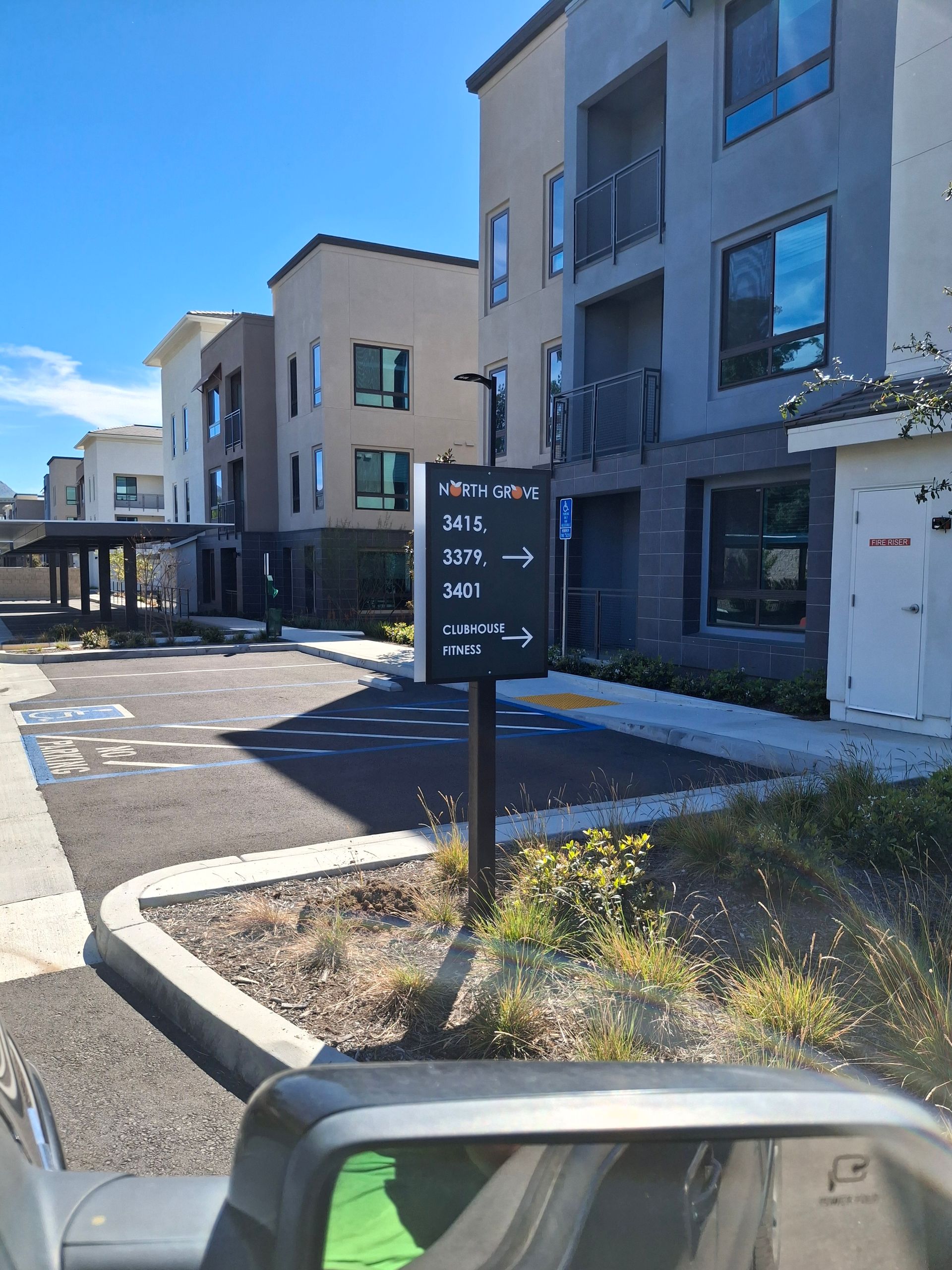 Modern apartment buildings with a black directional sign and parked car under a clear blue sky