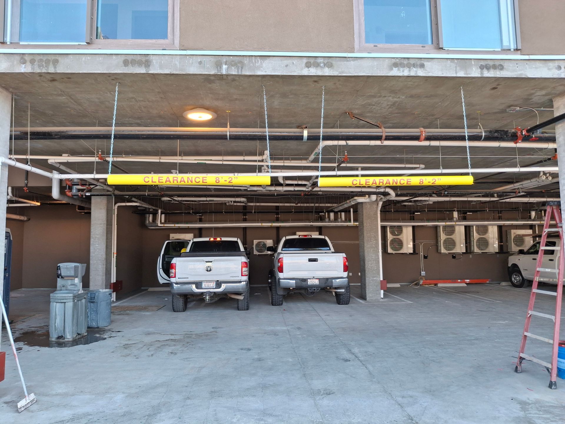 Parking garage with two pickup trucks parked under an overhang and a ladder on the right