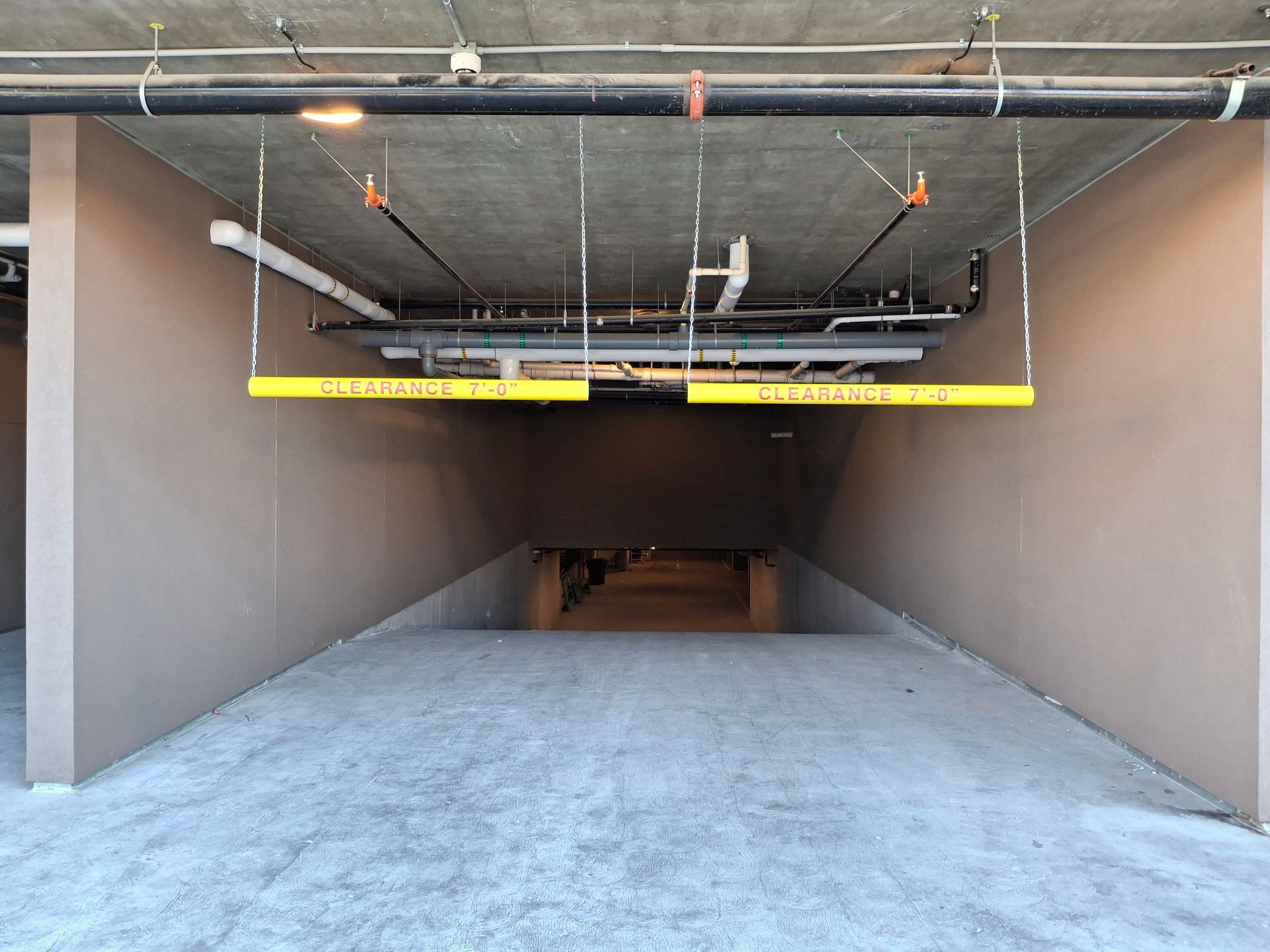 Empty parking garage entrance with low overhead pipes and a yellow clearance bar