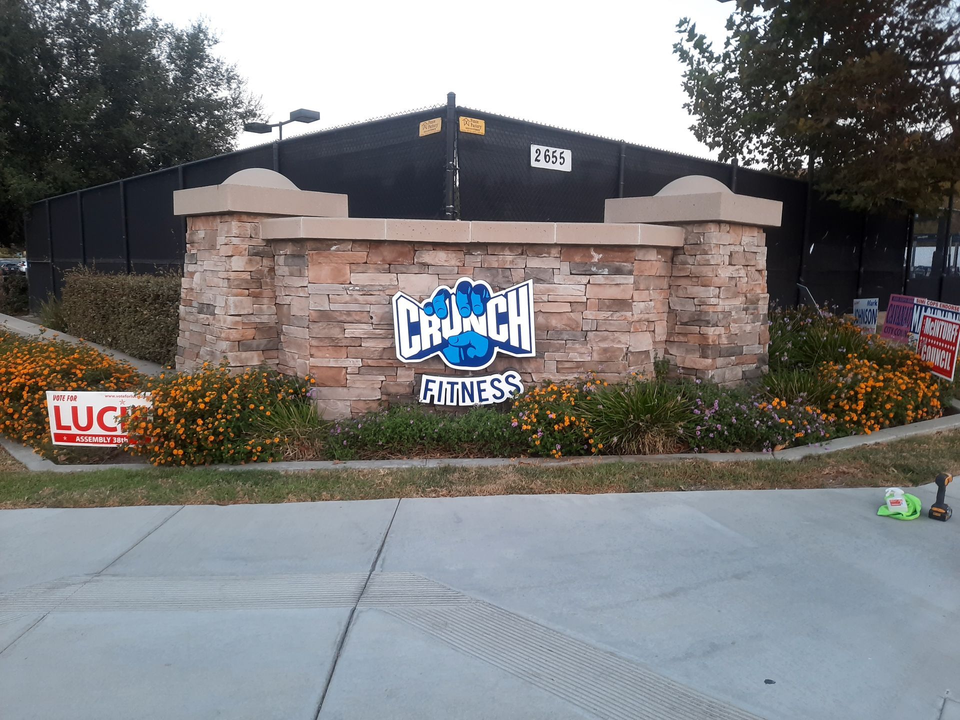 Crunch Fitness entrance with stone sign, flowers, and sidewalk in front of a dark building