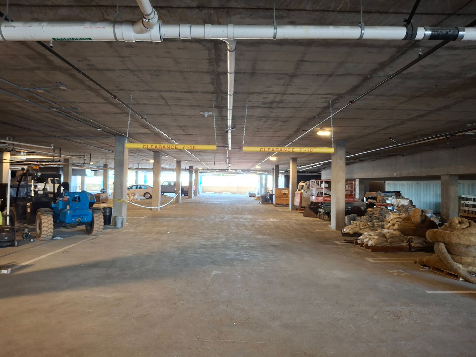 Empty underground parking garage with concrete ceiling, support columns, and construction materials stored along the sides