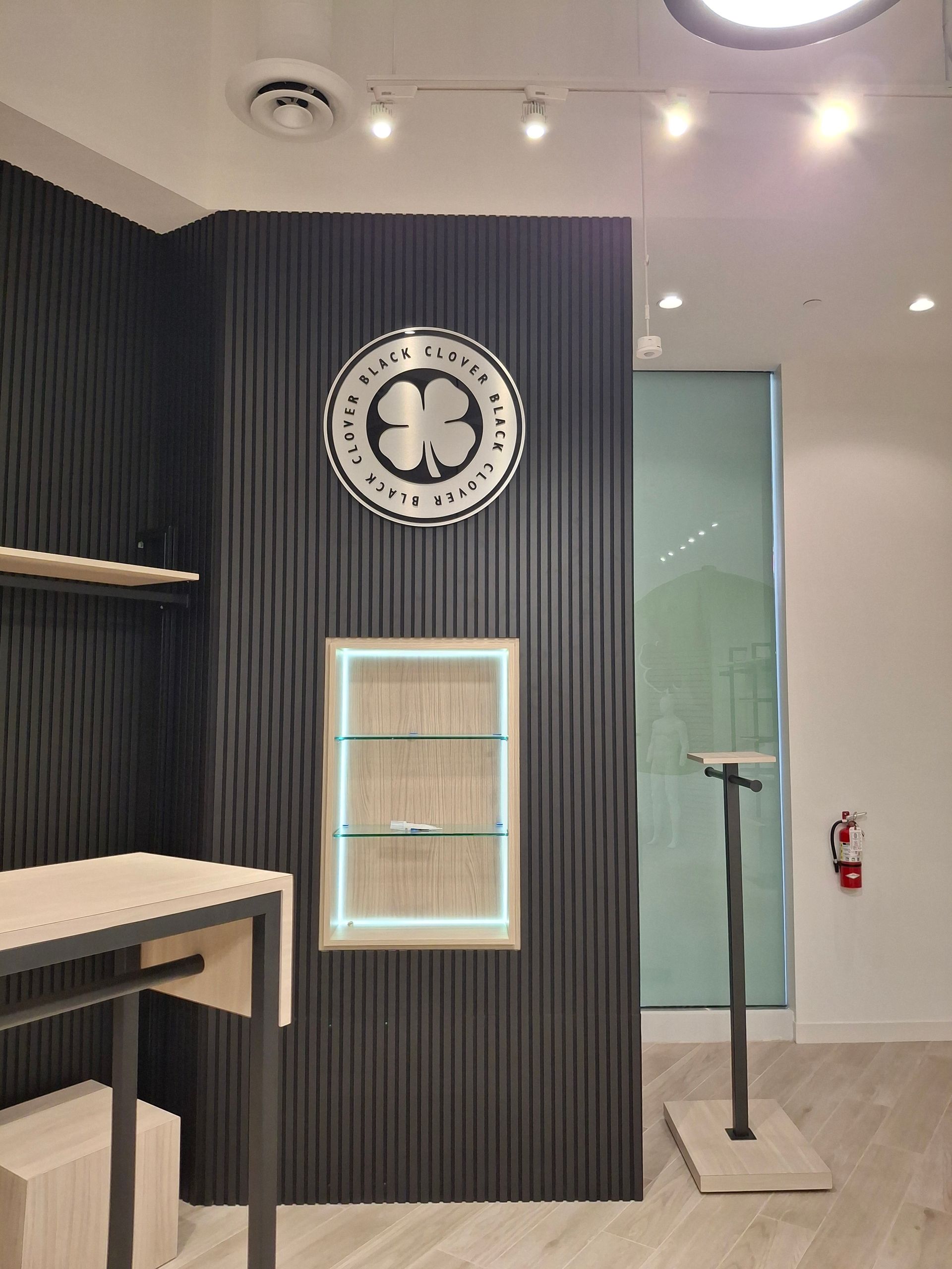 Modern minimalist lobby with a black slat wall, round clock, illuminated display niche, and glass door.