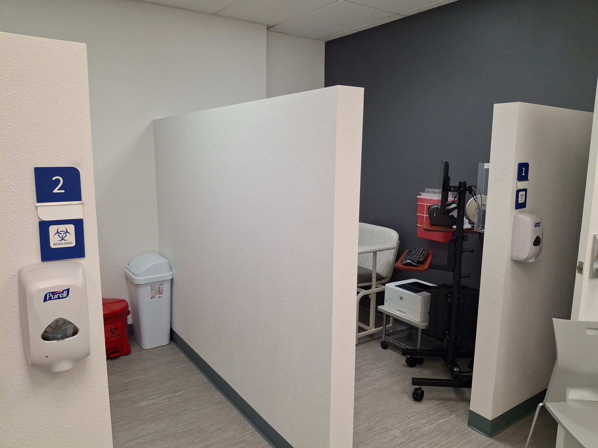 Office cubicle hallway with white partitions, dark wall, and a chair by a workstation on the right.