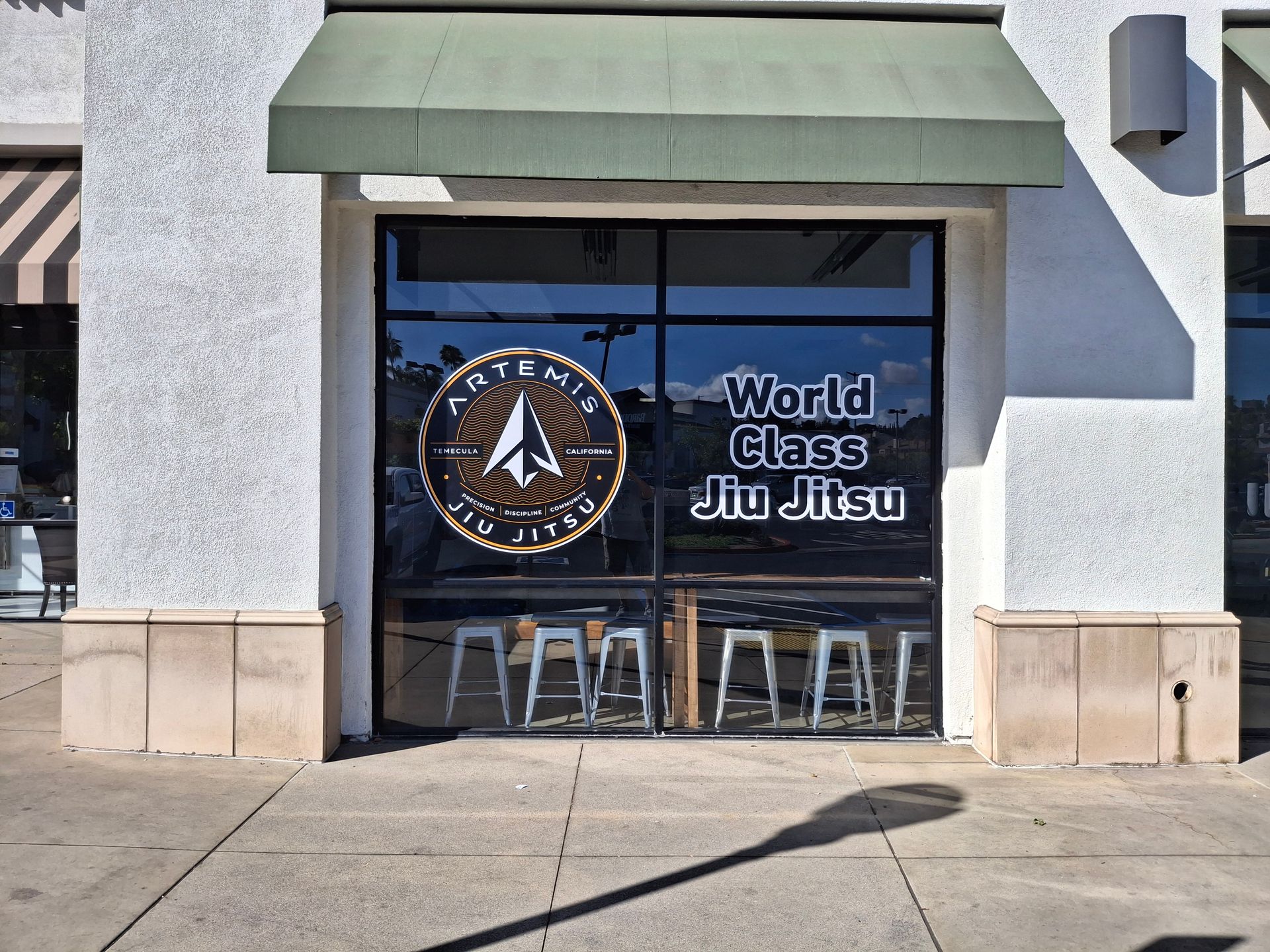 Storefront window with “World Class Jiu Jitsu” sign and martial arts logo under a green awning.
