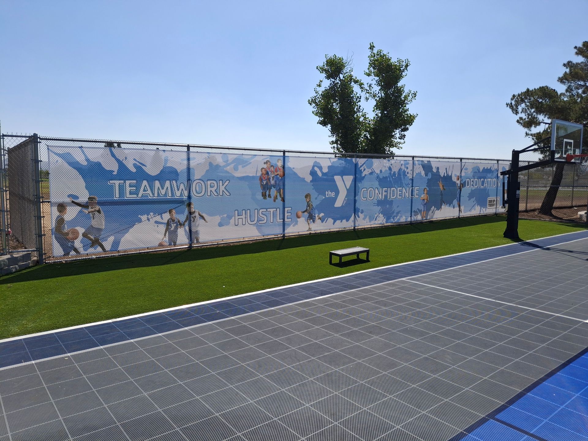 Outdoor pickleball court with blue surface, patterned walkway, and a mural fence under a clear sky