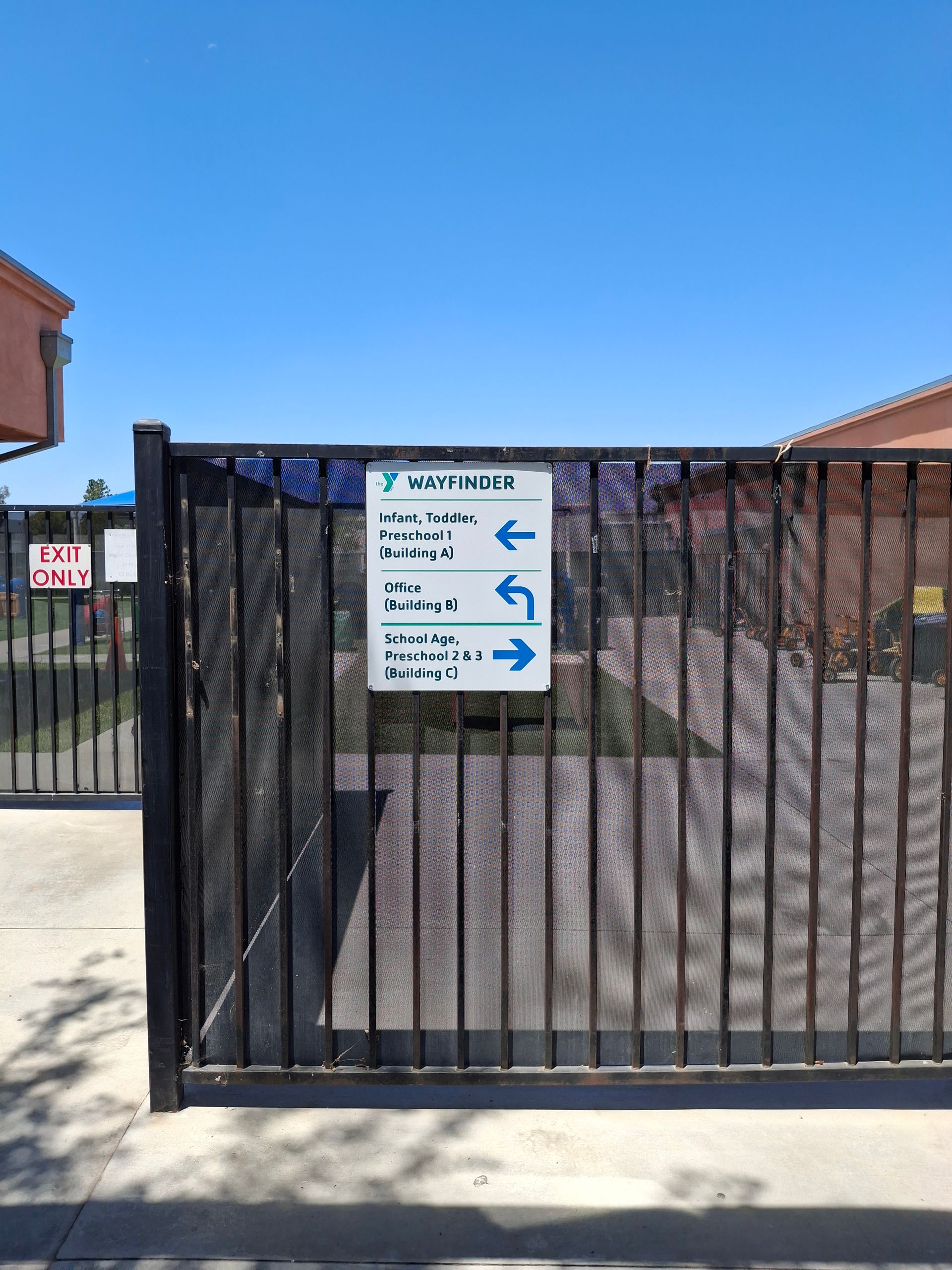 Black metal gate with a white directional sign in front of a building under a clear blue sky.