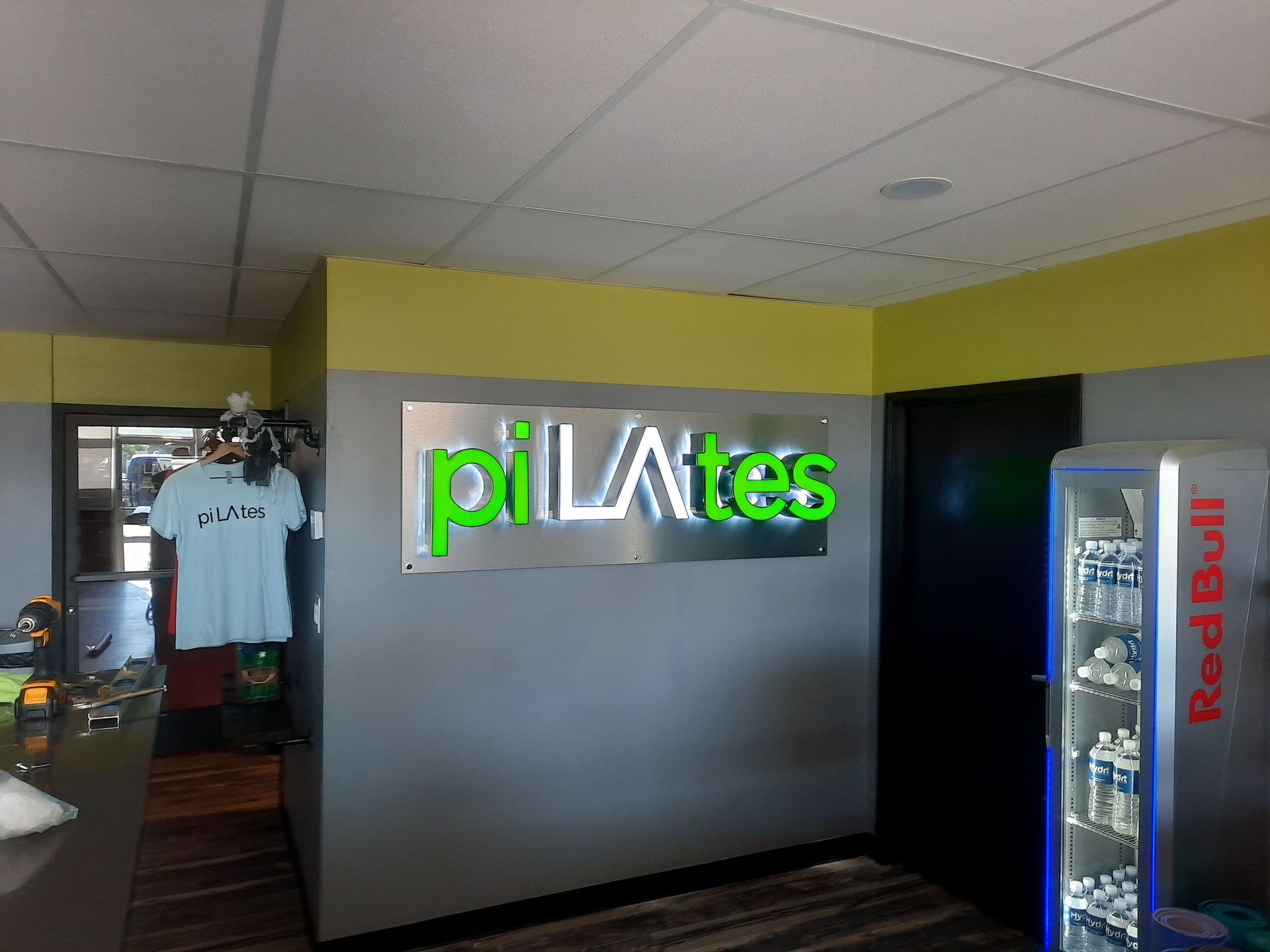 Pilates studio entrance with neon sign on a gray wall and a vending machine nearby