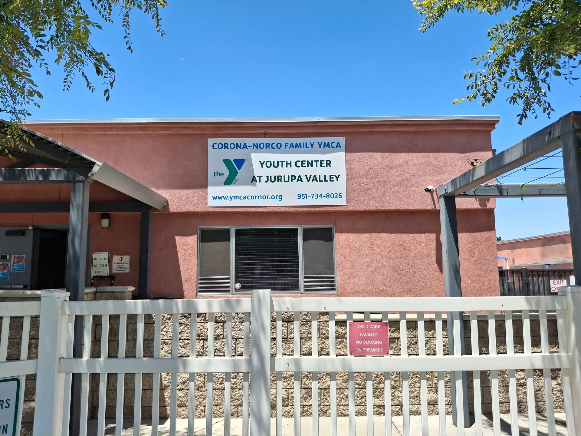 Front view of a youth center building with a white fence and pink walls under a blue sky.