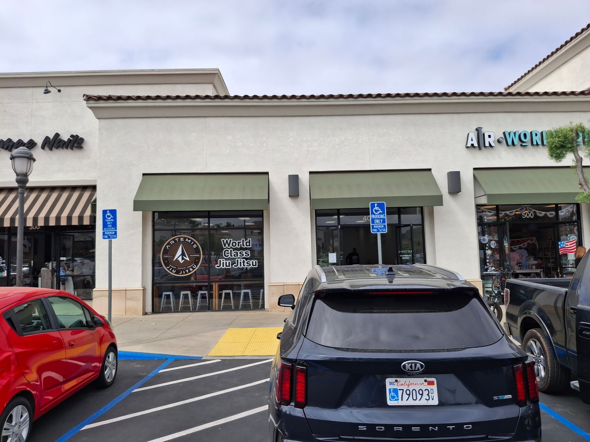 Storefronts with green awnings and parked cars in a shopping center lot
