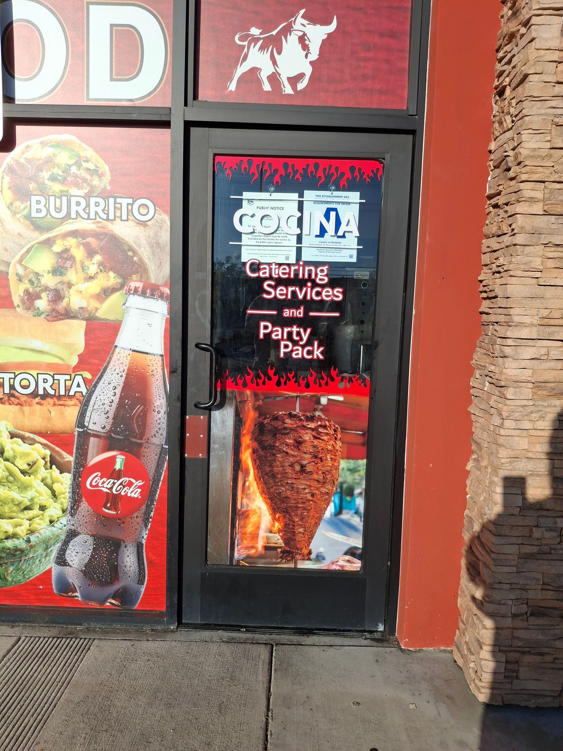 Restaurant entrance with black door and window signs for catering, services, party trays, and pickup.