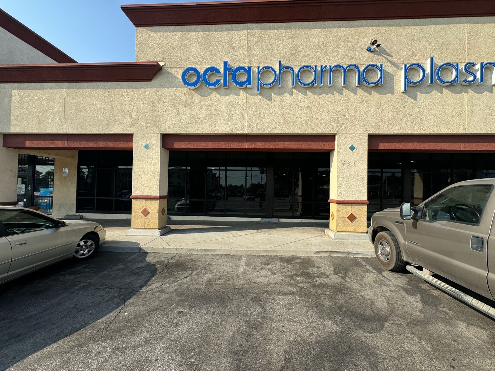 Storefront of Octapharma Plasma in a strip mall with parked cars outside
