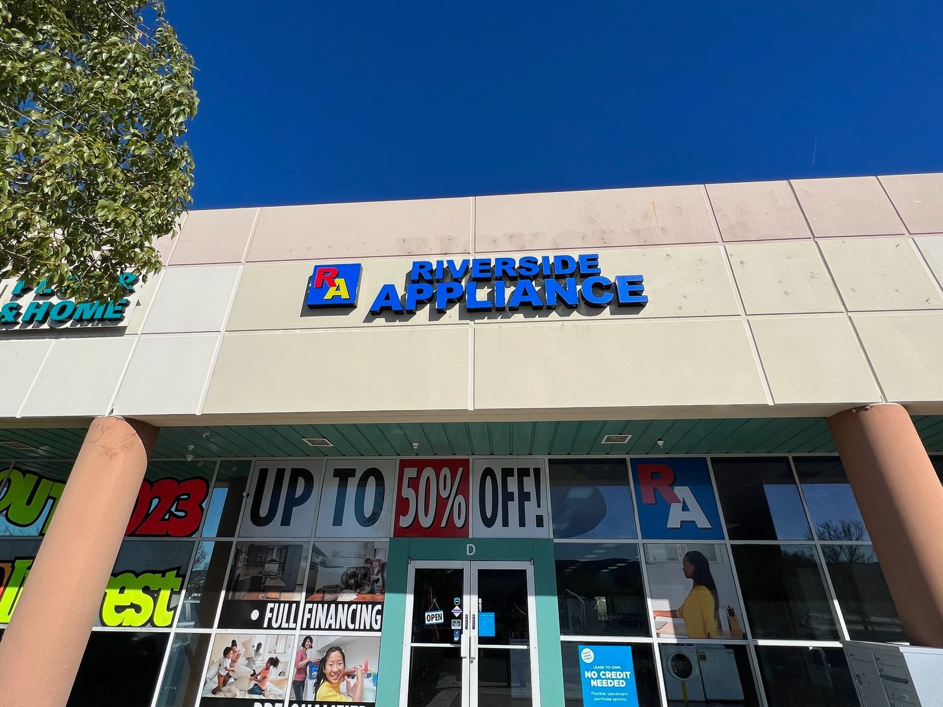 Storefront of American Appliance with a “UP TO 50% OFF” sale sign and glass entrance doors