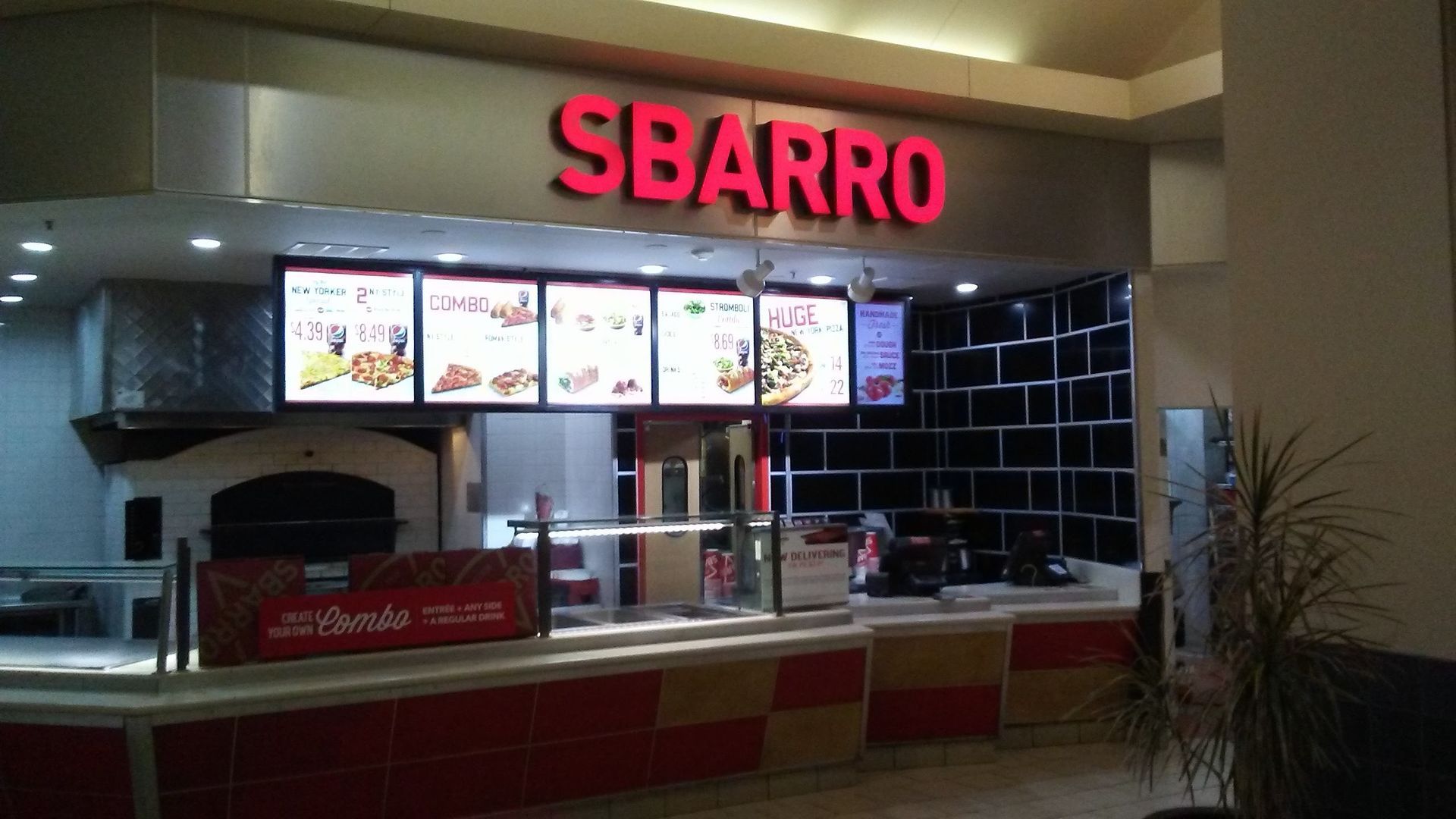 Sbarro pizza counter with red illuminated sign and menu boards in a mall food court
