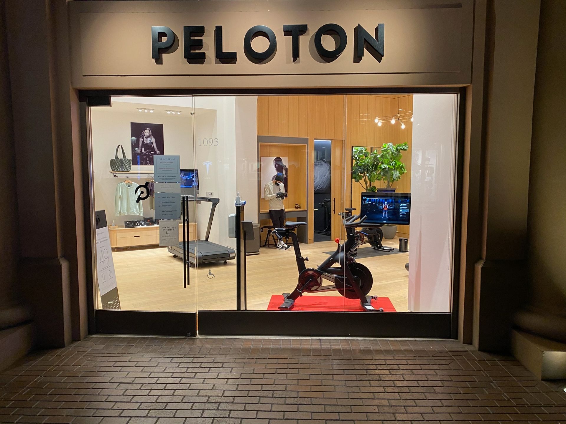 Peloton storefront with exercise bikes visible through large glass windows at night