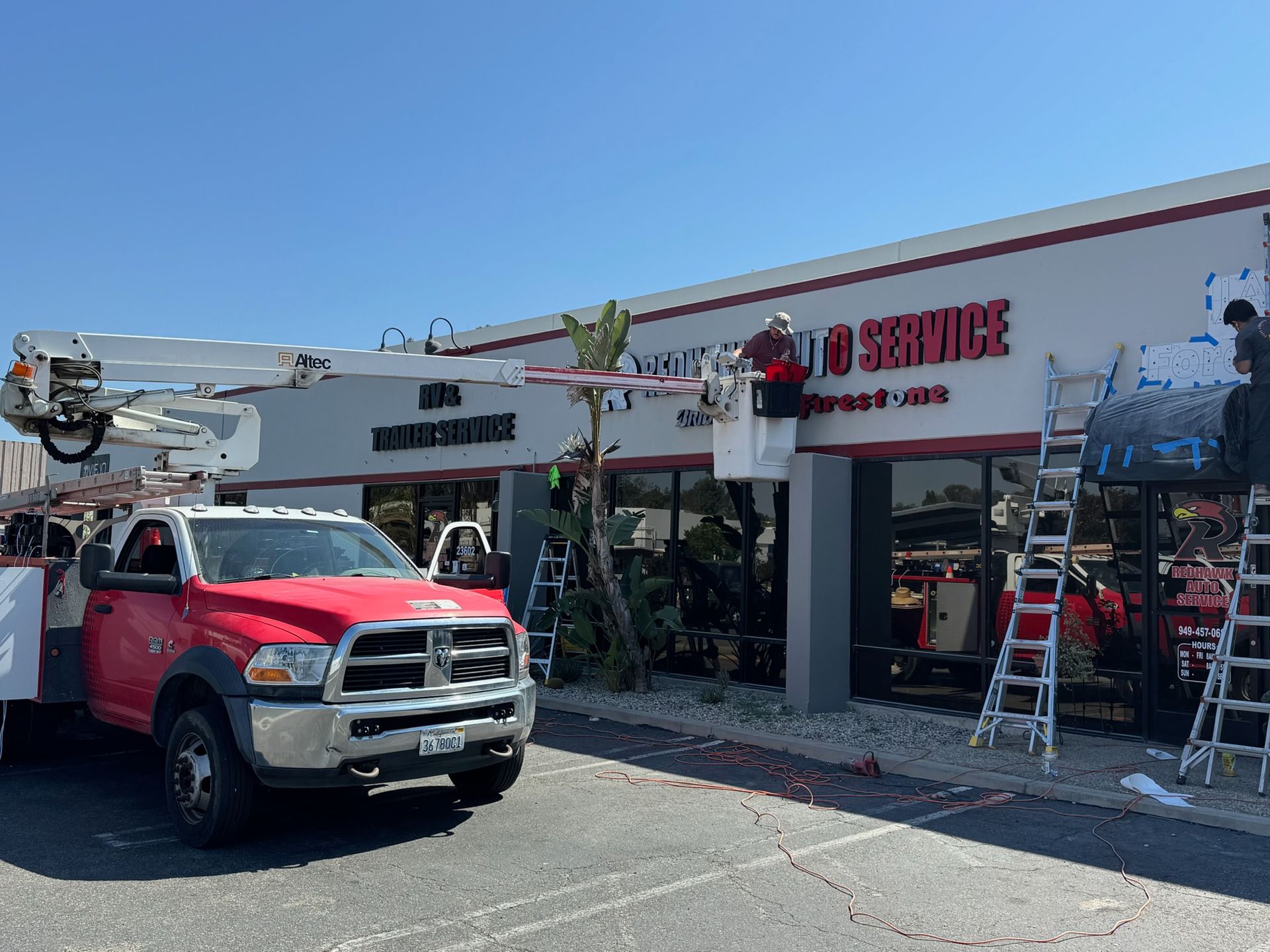 Red utility truck and ladder outside a Service Specialists storefront with workers and tools in front.