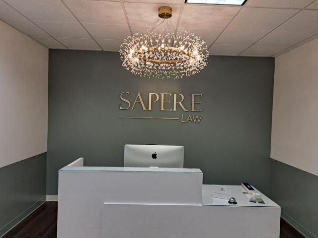 Minimalist office lobby with gray walls, a chandelier, and a front desk under the “SAPERE” sign