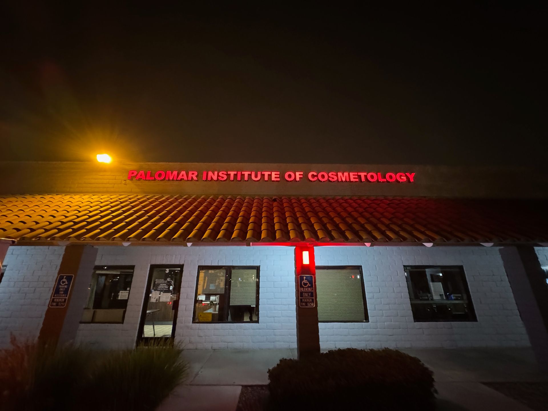 Night view of a lit building with red “... Institute of Cosmetology” sign above the entrance