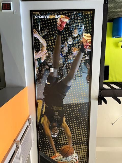 Person doing a handstand on a black cabinet with a basketball, indoors against a bright yellow wall.